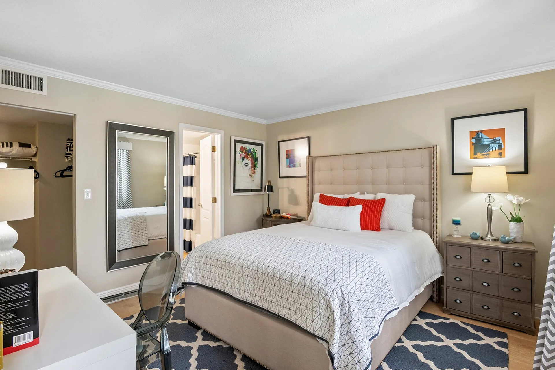 Inviting bedroom showcasing a plush bed with stylish red and white accents, elegant mirrored decor, and warm lighting.