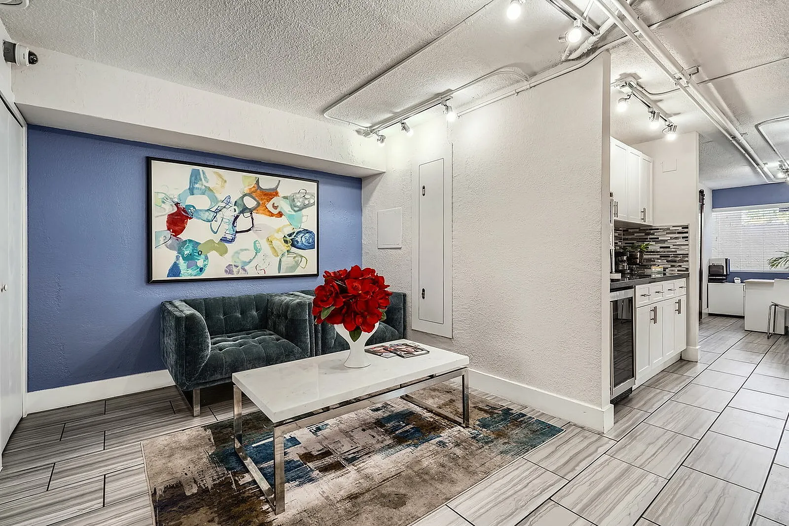 Chic apartment interior showcasing a modern lounge with a plush green sofa, vibrant abstract art, and sleek kitchen design.