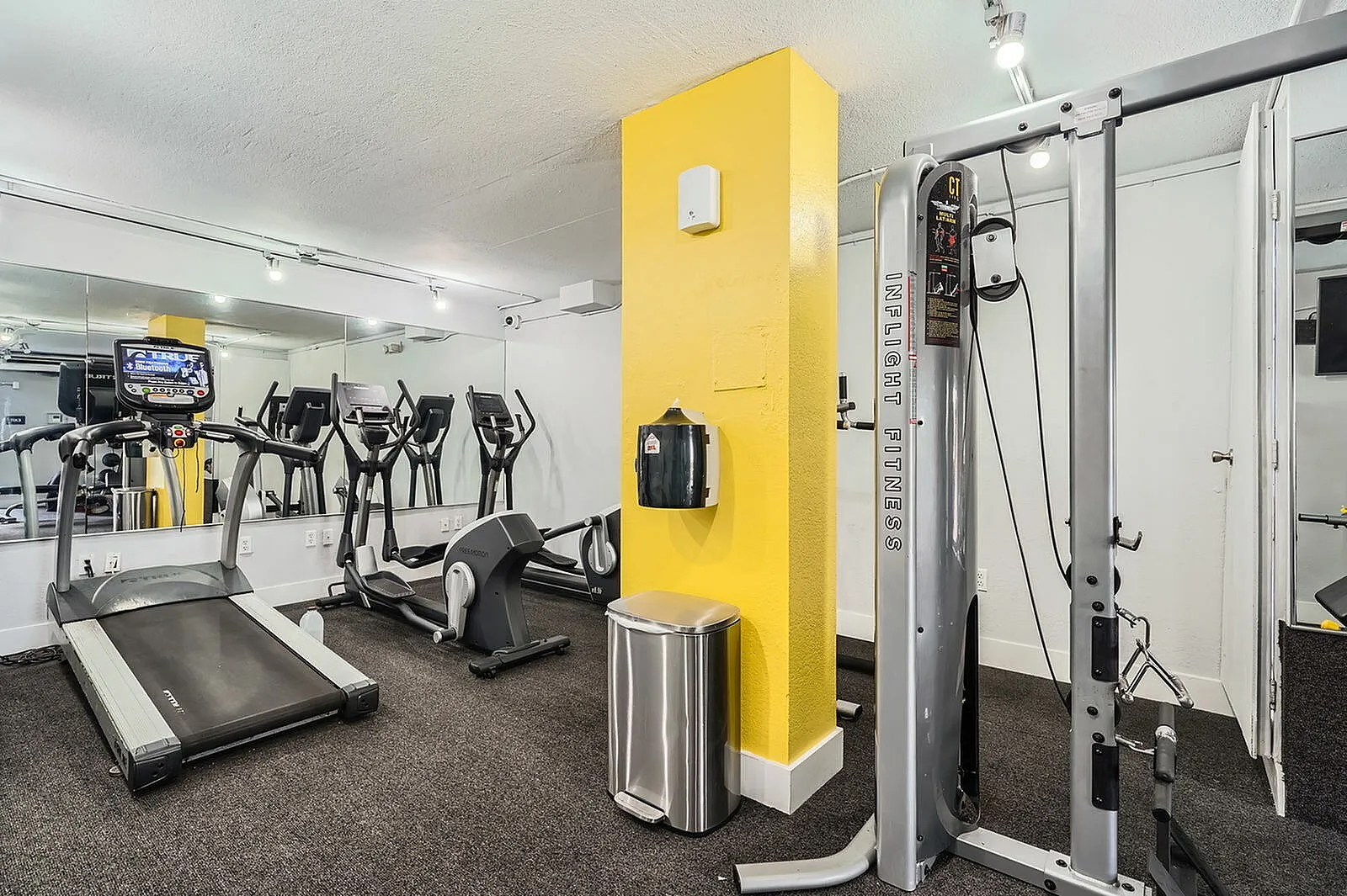 Modern fitness center featuring advanced gym equipment, mirrored walls, and bright yellow accents for an energetic workout ambiance.