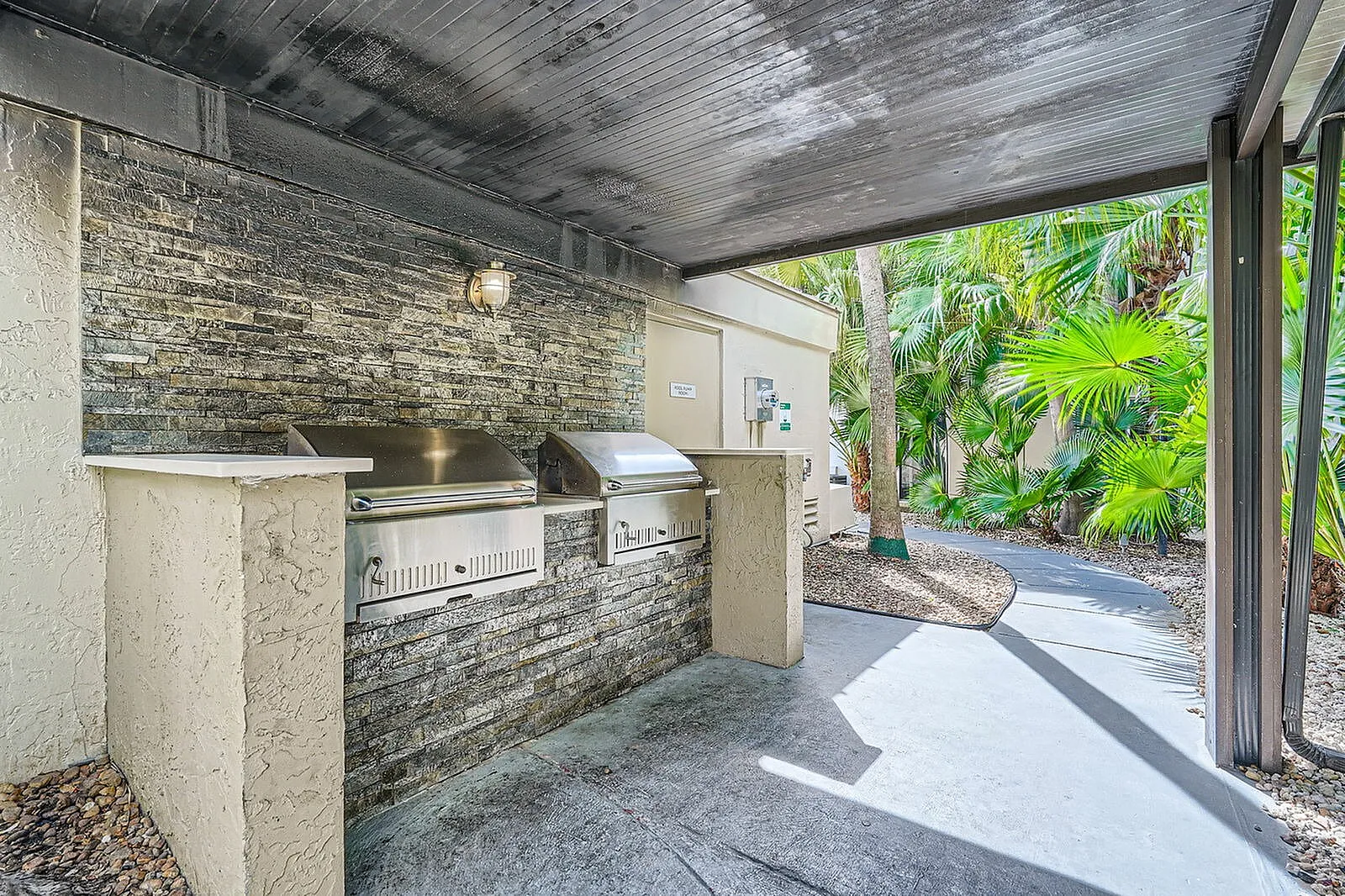 Inviting outdoor BBQ area with sleek stainless steel grills and lush tropical landscaping for a perfect alfresco experience.