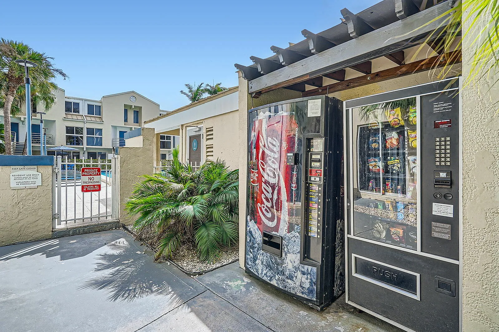 Charming outdoor view of apartment complex featuring modern architecture and convenient vending machines, surrounded by lush greenery.