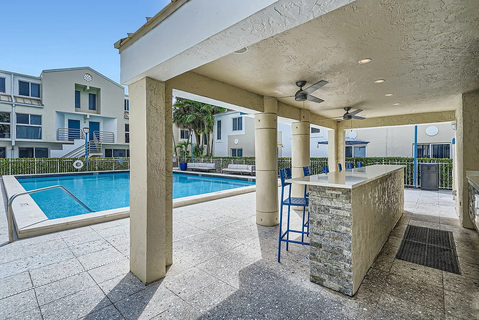 Inviting outdoor area featuring a sparkling pool, covered bar with high stools, and modern apartment backdrop.