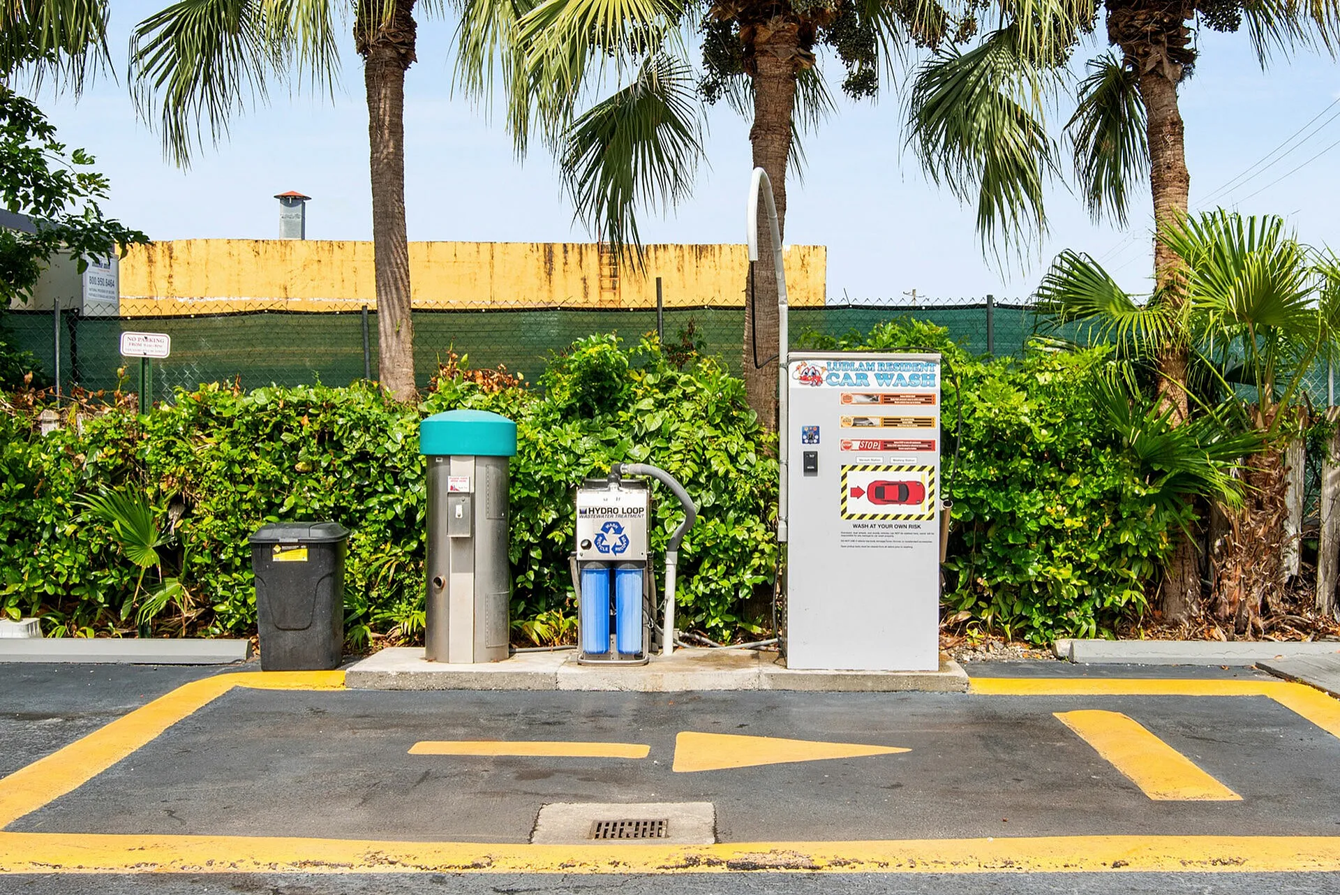 Vibrant car wash station surrounded by lush greenery and palm trees under a clear blue sky.