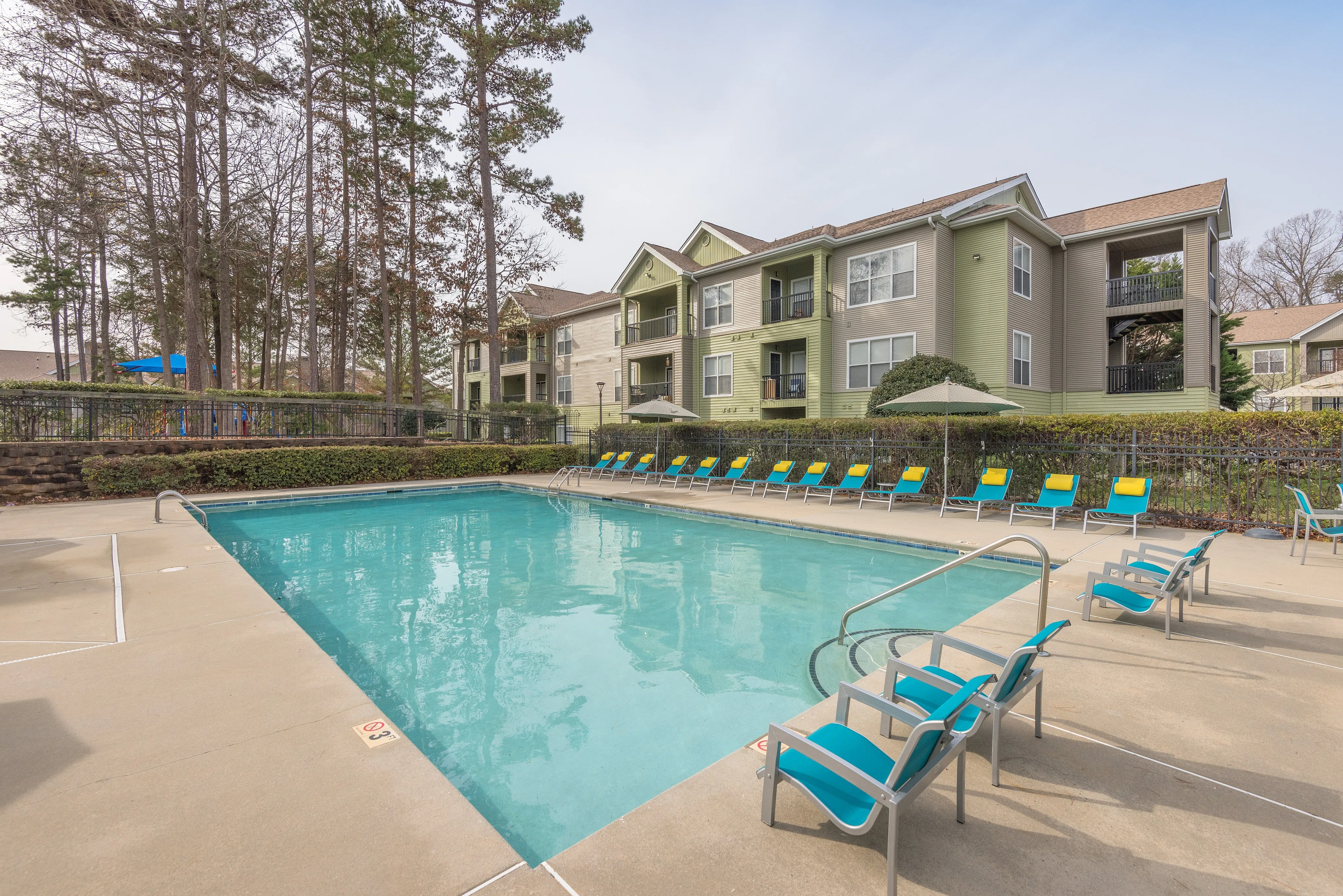 Luxurious apartment complex featuring a sparkling outdoor pool surrounded by modern lounge chairs, set against a backdrop of elegant multi-story buildings and lush trees.