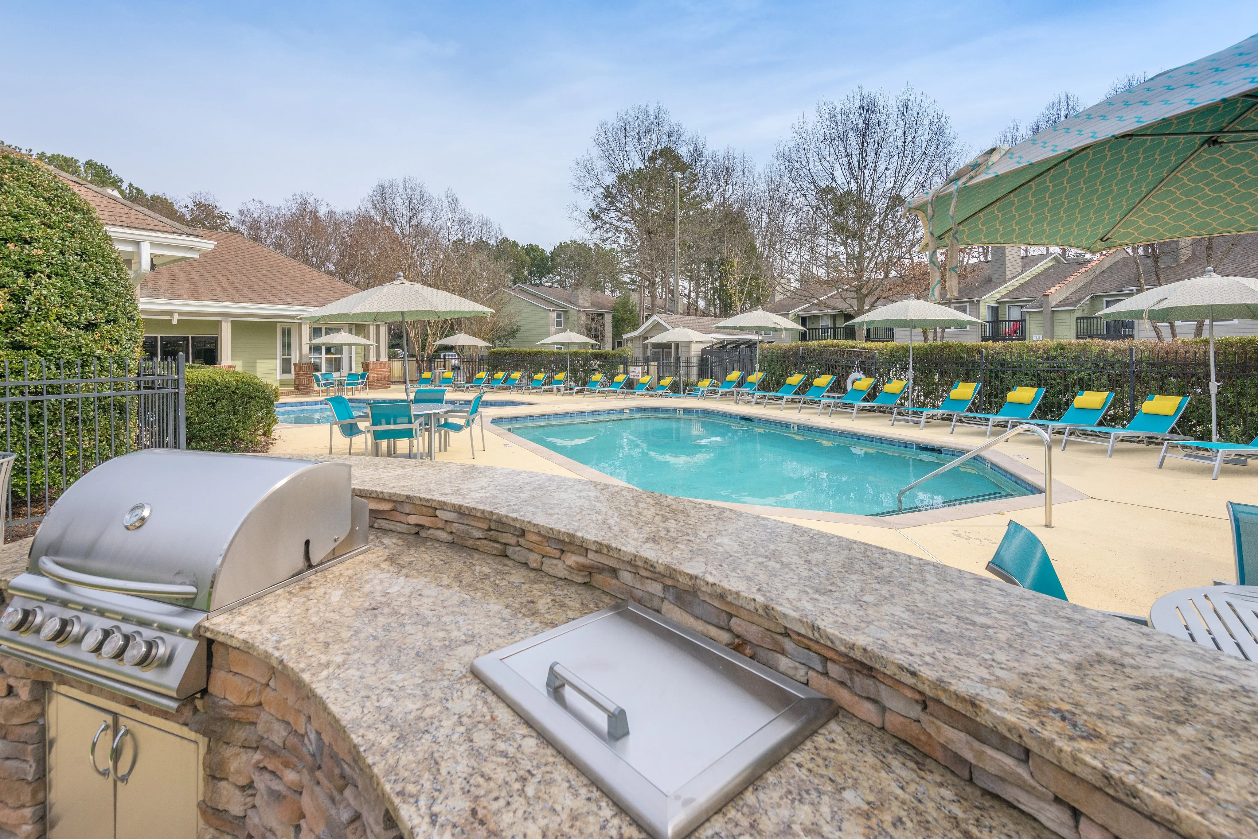 Luxurious outdoor area featuring a sparkling pool surrounded by vibrant lounge chairs, shaded by elegant umbrellas, and complemented by a sleek built-in barbecue grill.