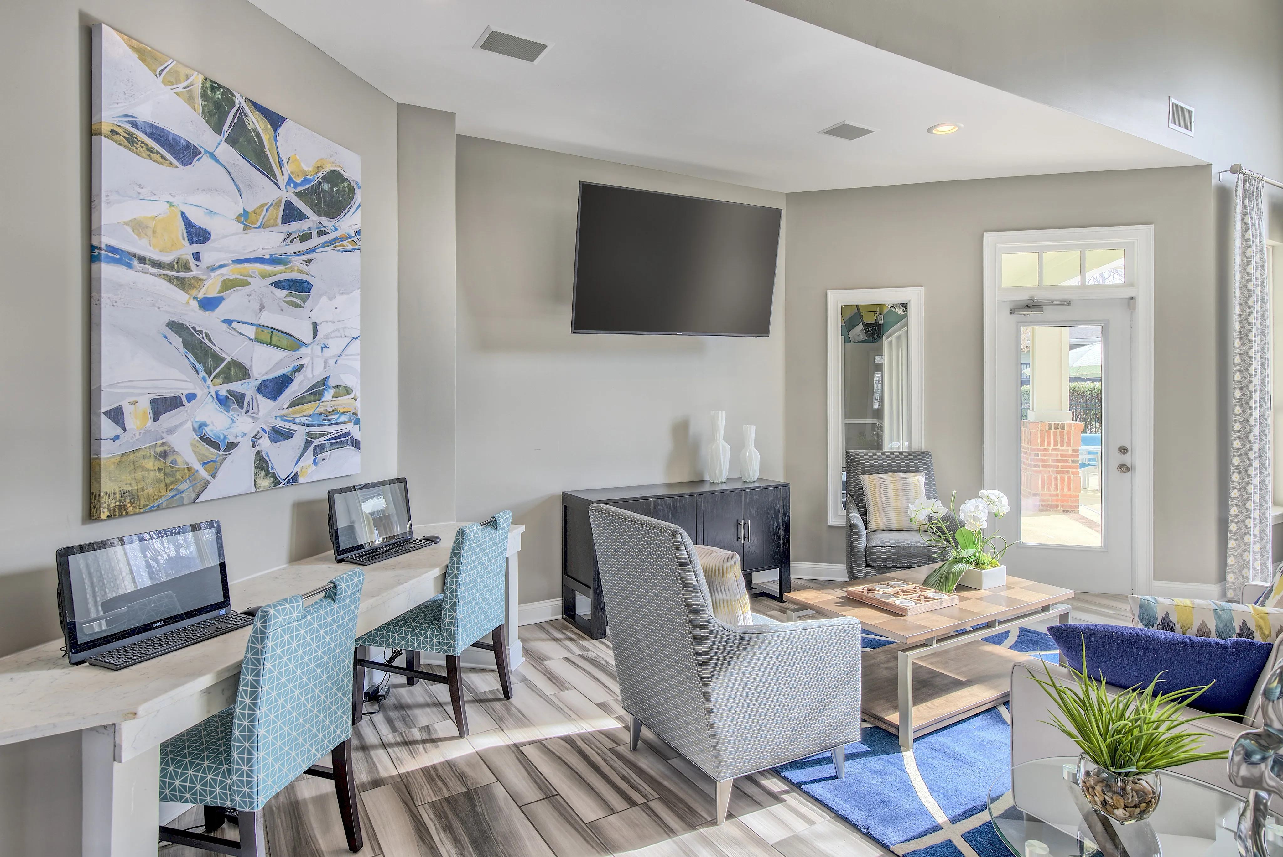 Bright and modern living space with chic seating, a vibrant abstract painting, and a work area with two laptops, enhanced by natural light and stylish decor.