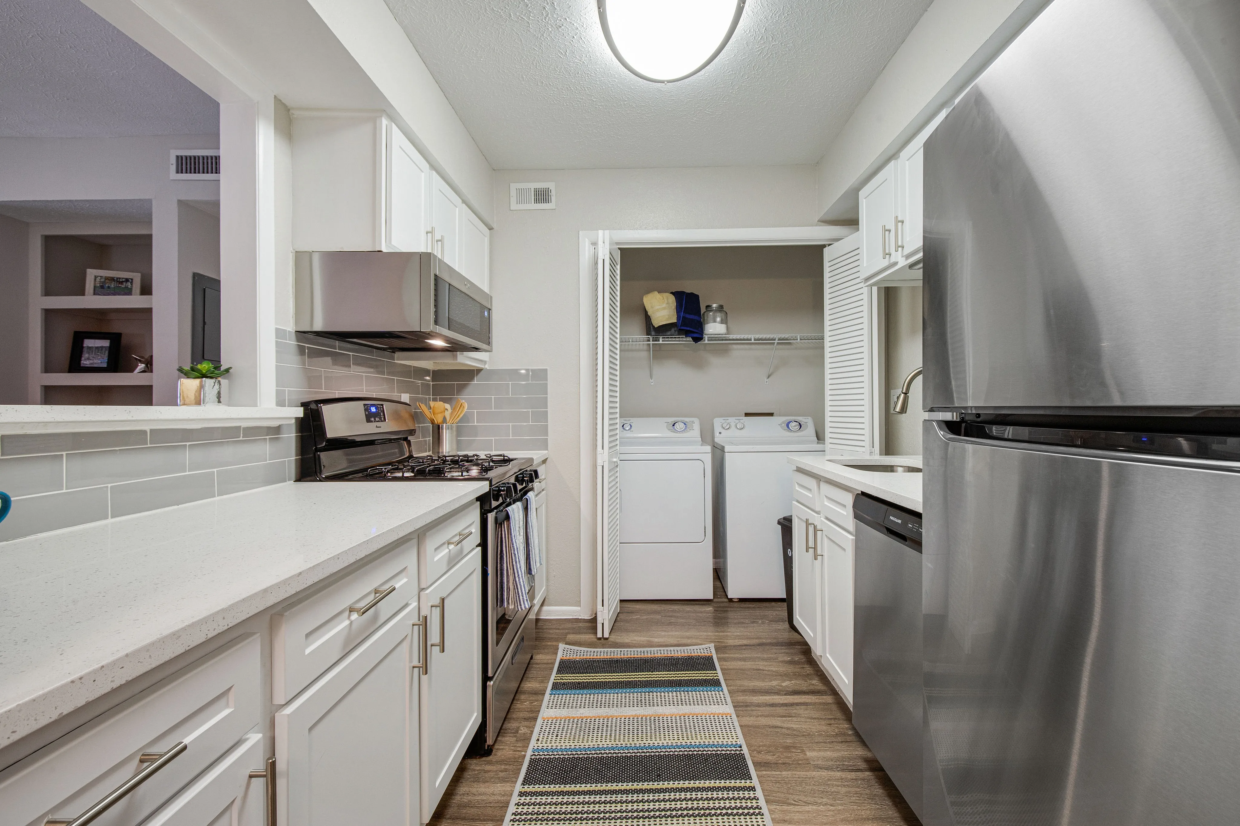 Modern kitchen with sleek stainless steel appliances, elegant white cabinetry, and an in-unit laundry area for added convenience.