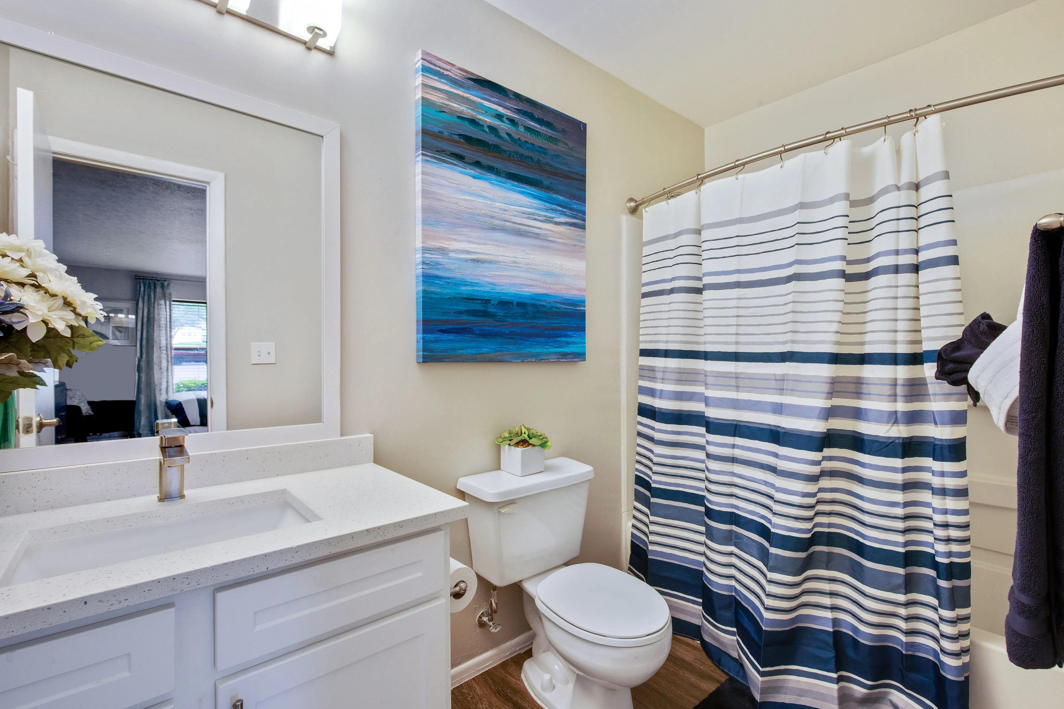 Bright and inviting bathroom with modern fixtures, featuring a stylish blue-themed painting and a striped shower curtain.