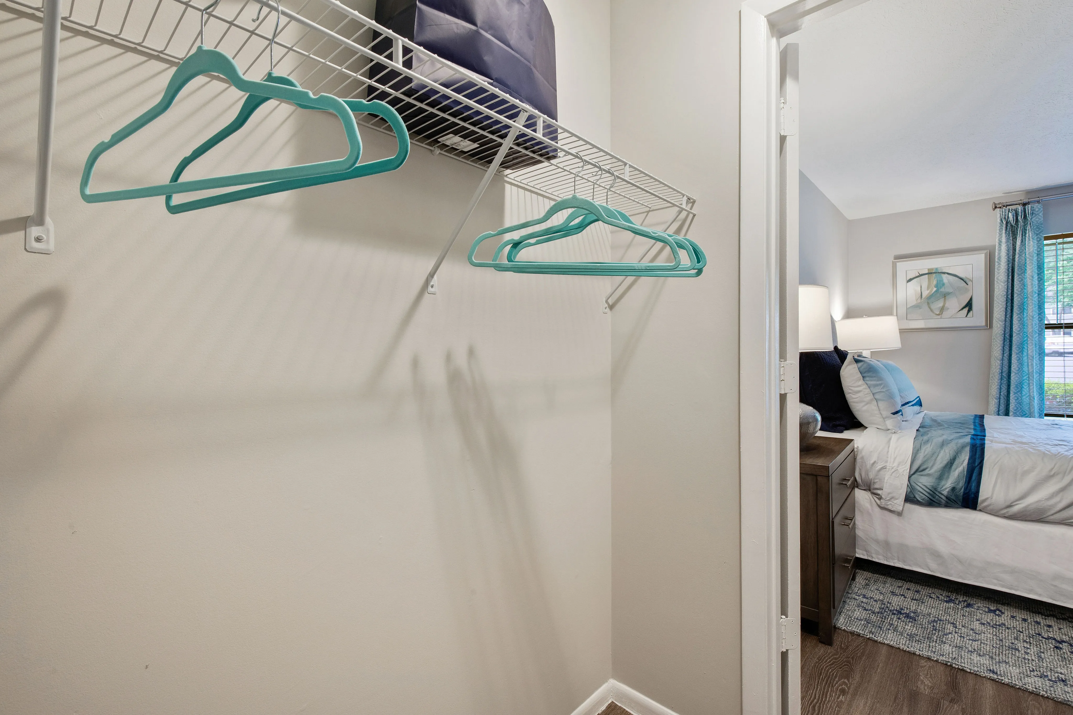 A closet with a shelf and partial views of a bedroom with a bed and a window at The Madison apartments in Charlotte, NC.
