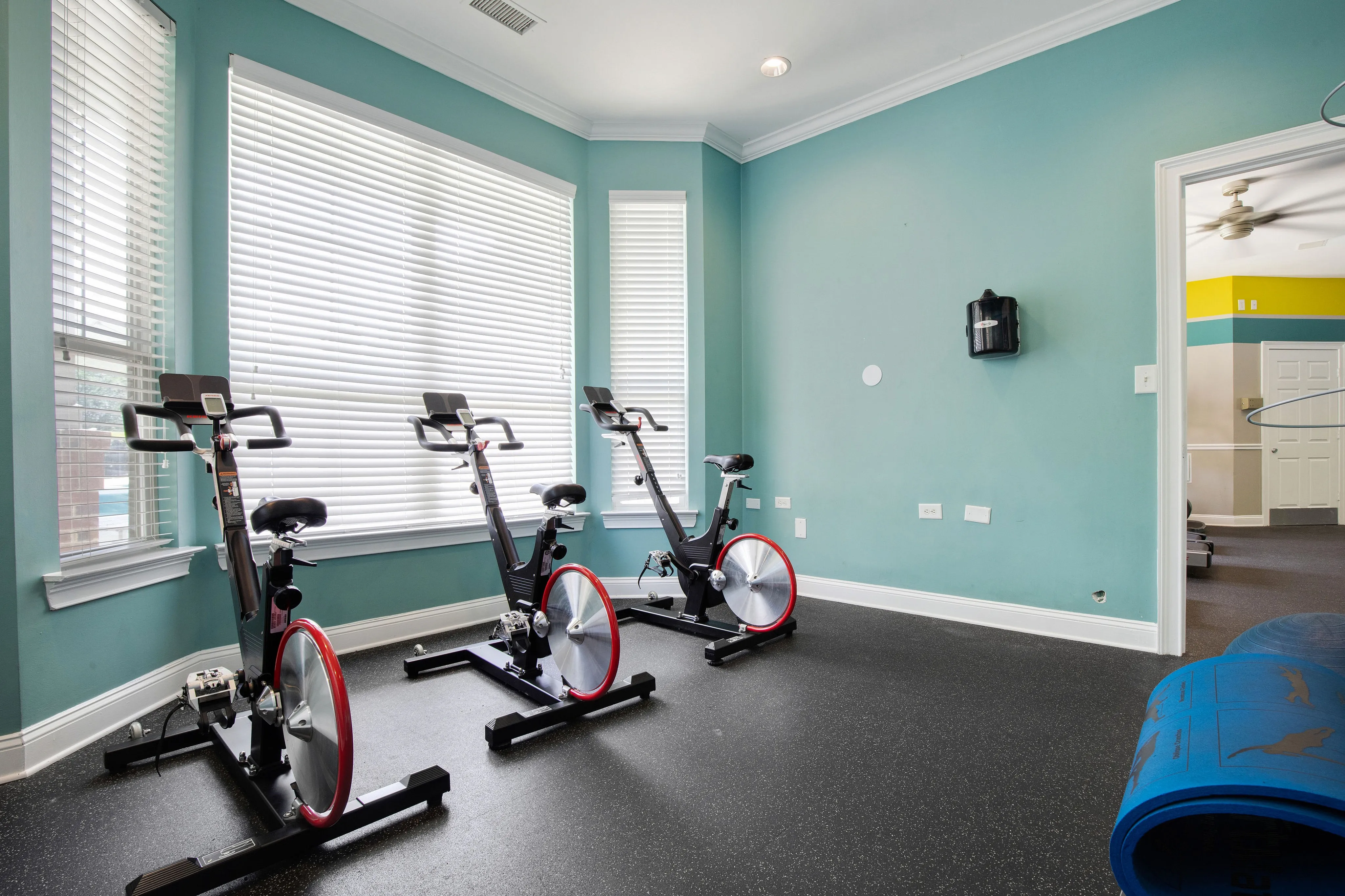 Bright home gym with three modern stationary bikes against a turquoise wall, perfect for an energetic workout.