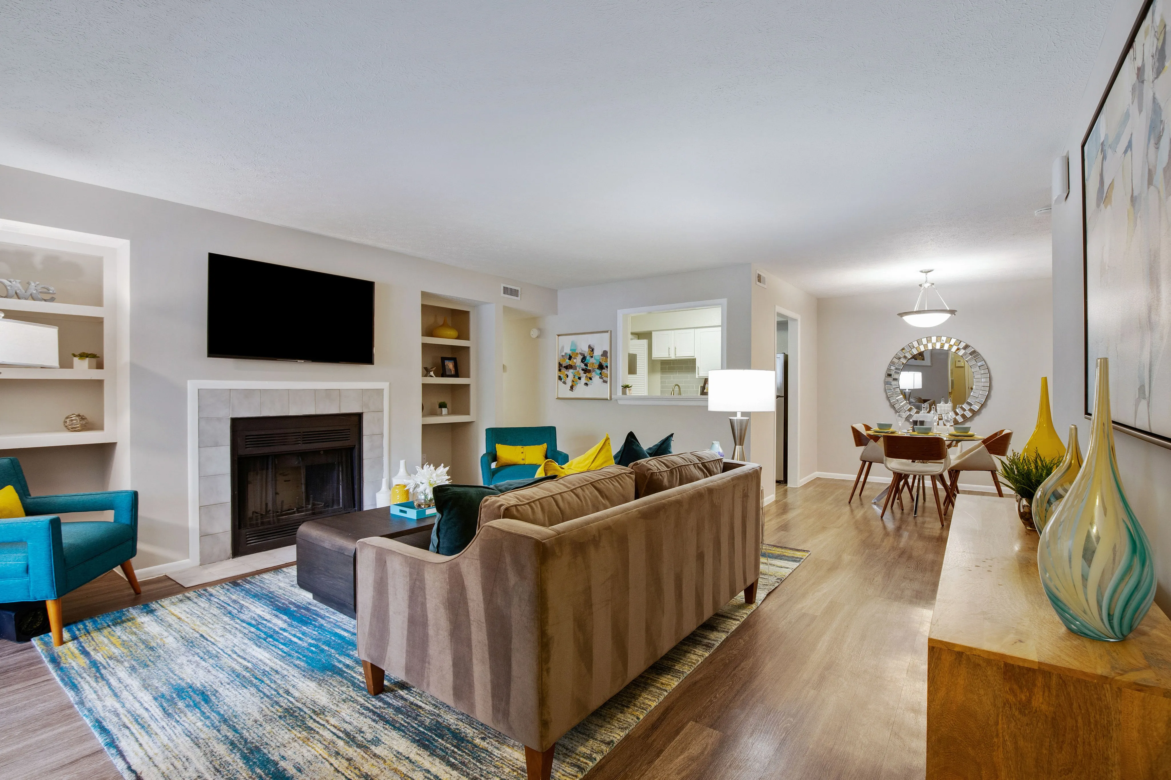 A living room with a couch and a flatscreen television, a dining area with a table and chairs, and a kitchen at The Madison apartments for rent in Charlotte, NC.