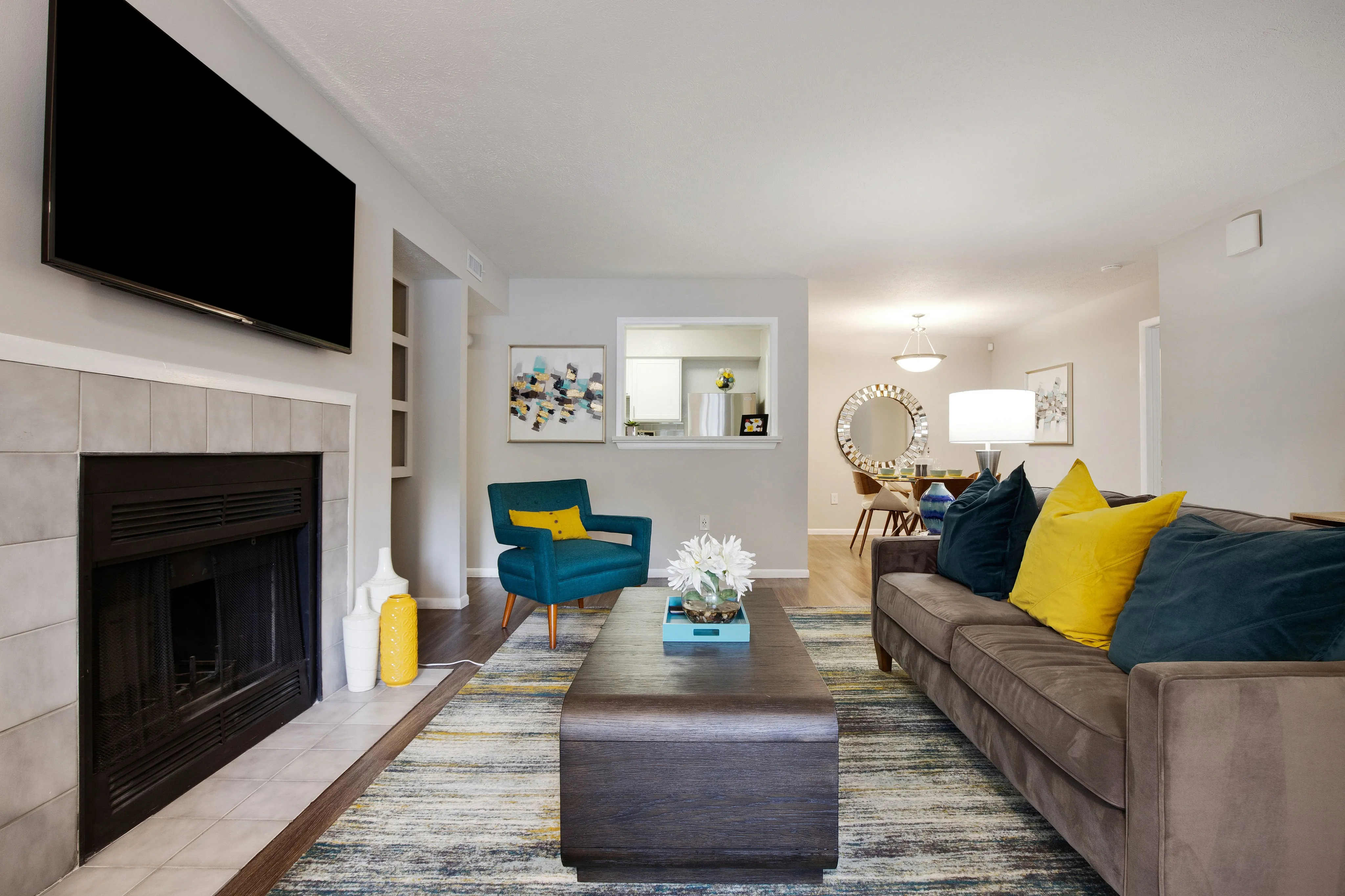 A living room with a couch, chairs, a coffee table, a flatscreen television, and a fireplace, with views of a dining area at The Madison apartments near Uptown Charlotte.