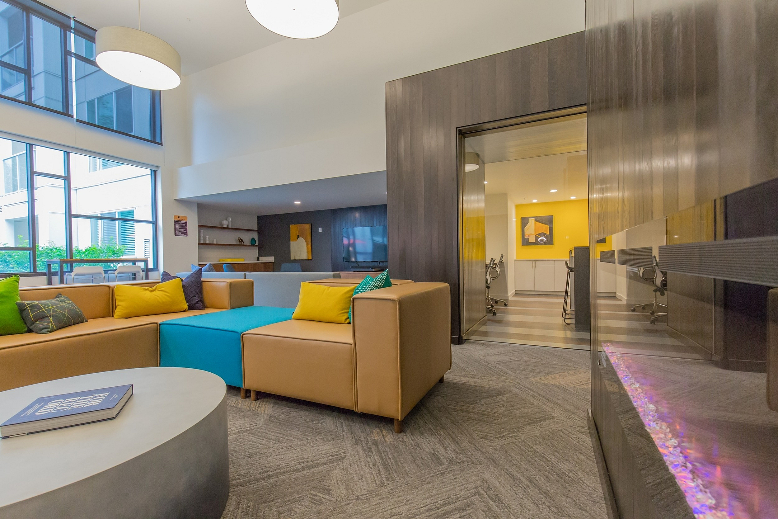 Contemporary lounge area with colorful seating, modern lighting, and a cozy study nook, bathed in natural light from large windows.
