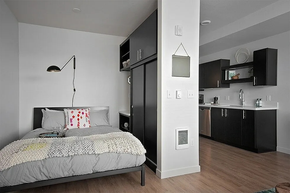Contemporary studio apartment showcasing a cozy bedroom area adjacent to a sleek modern kitchen with stylish dark cabinetry.