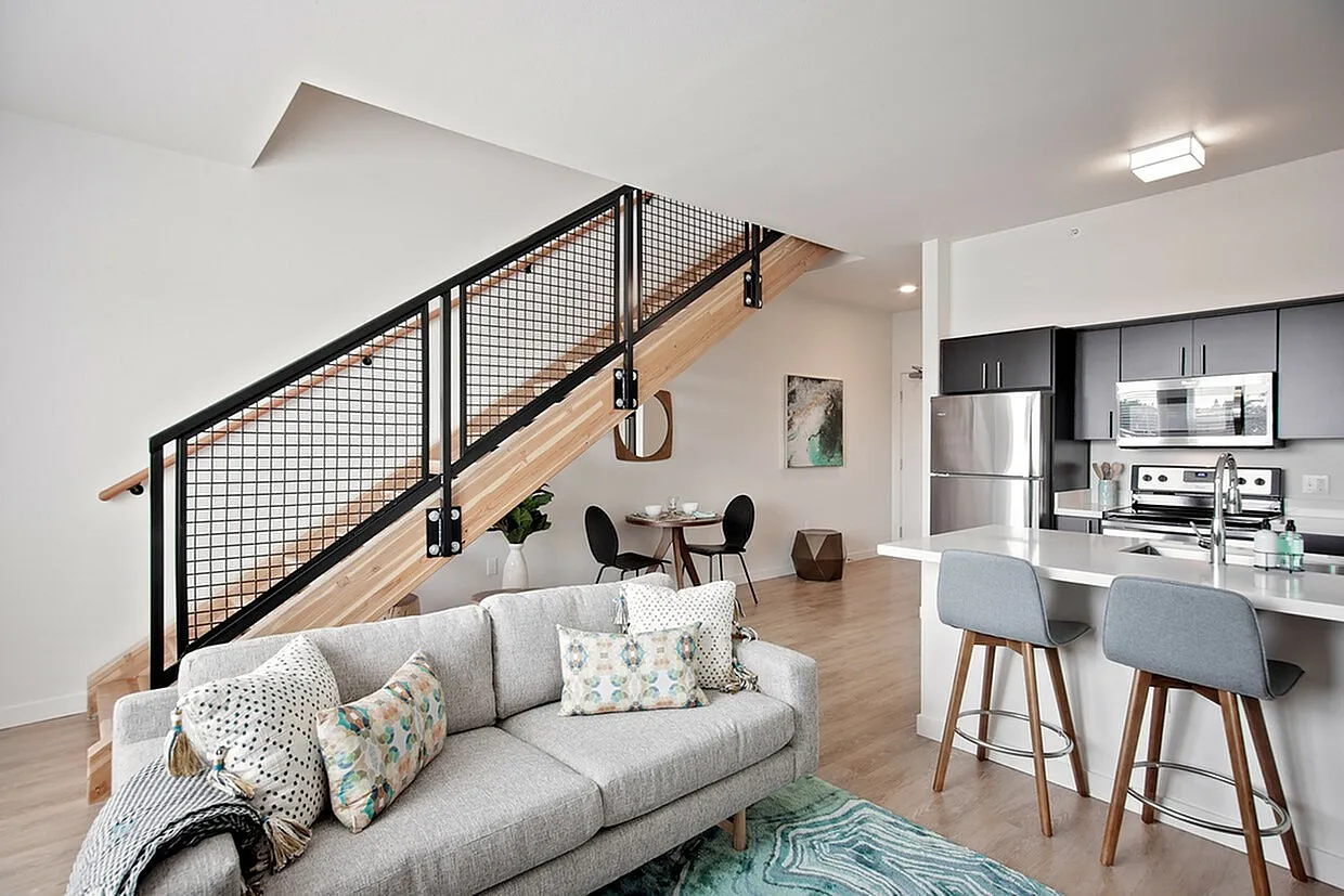 Modern open-concept living space with sleek kitchen, cozy sofa, and stylish staircase, perfect for contemporary living.