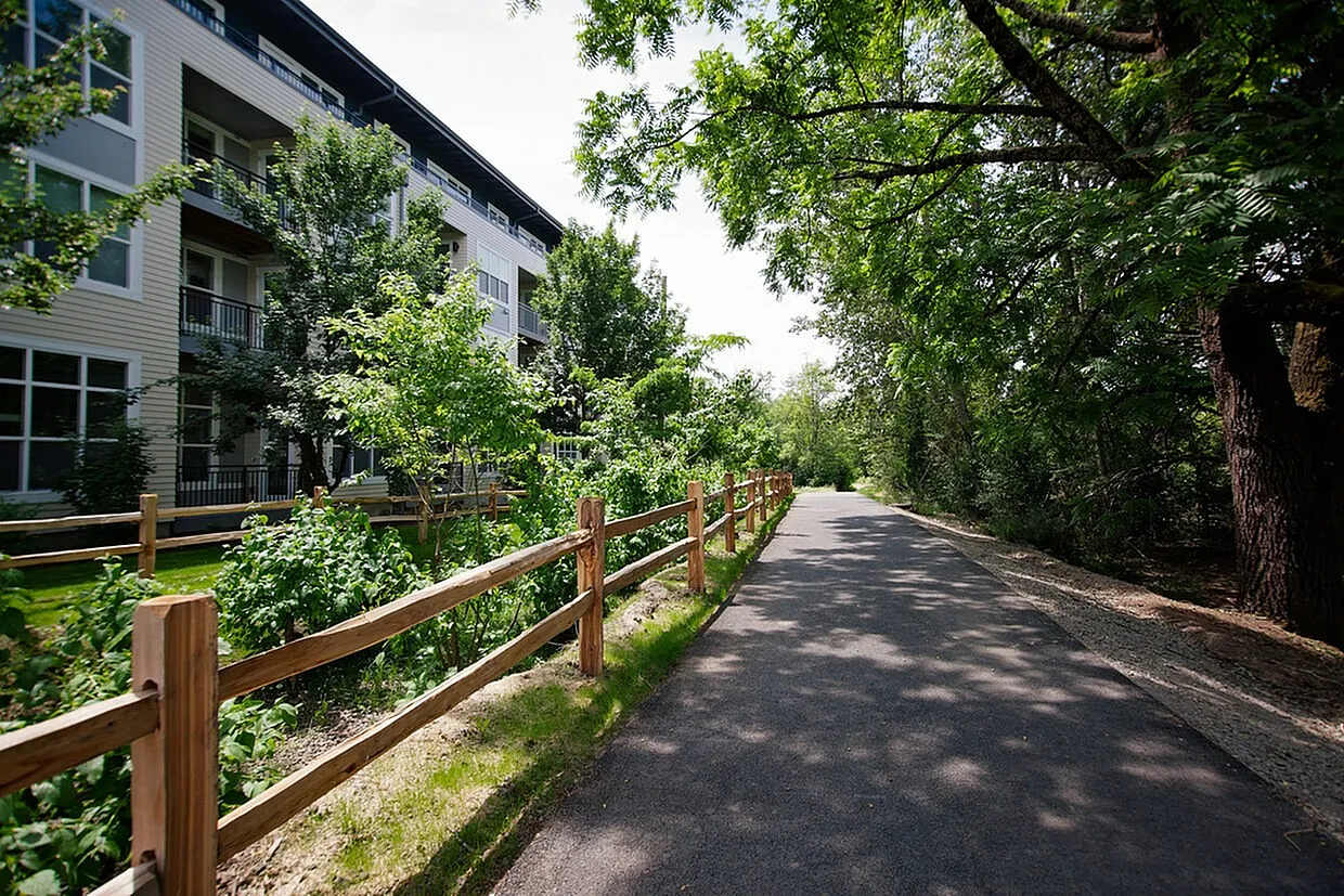 Charming apartment building nestled by a serene pathway and lush greenery, perfect for nature lovers.