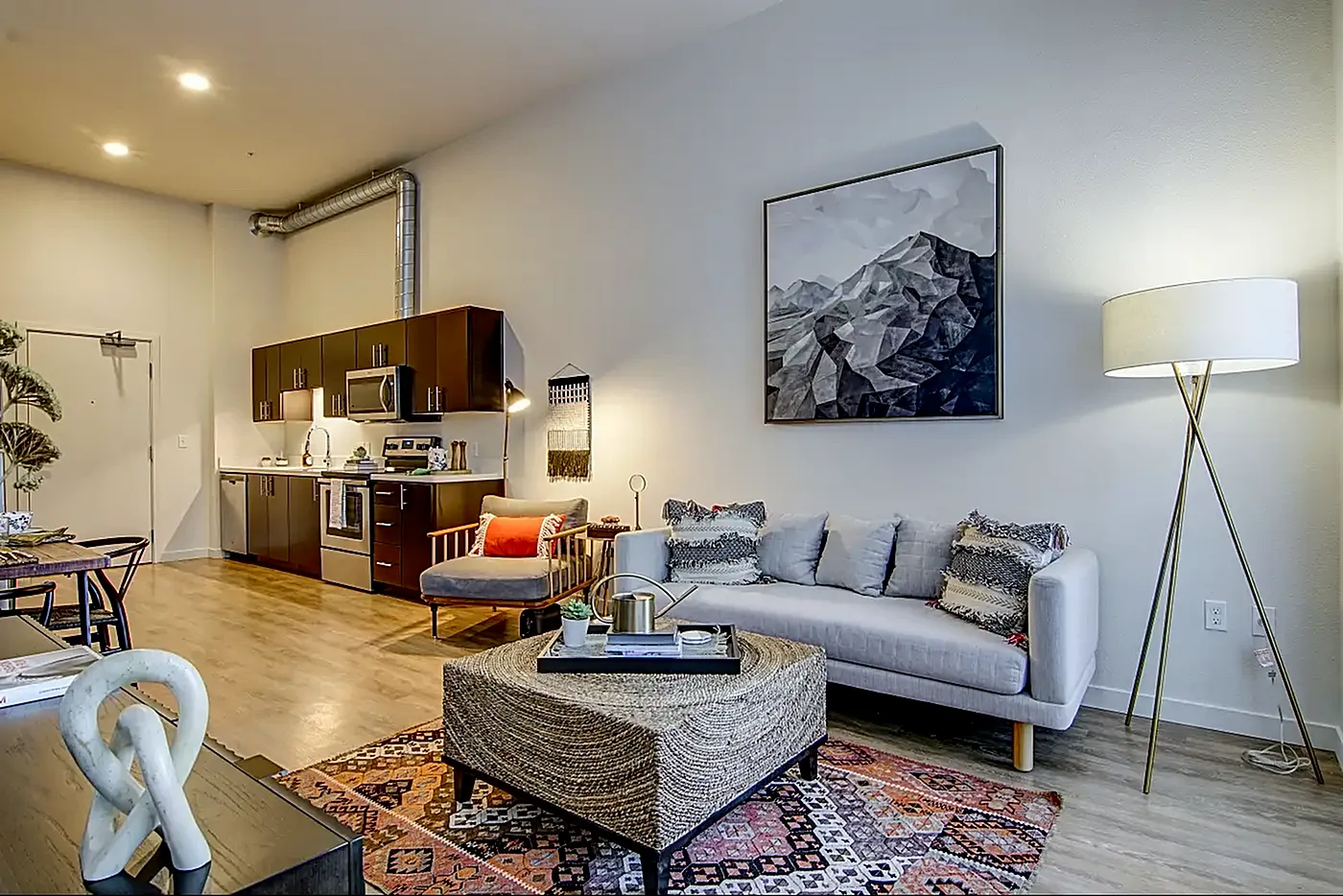 Modern open-concept living room with stylish decor, cozy seating, artistic wall art, and a sleek kitchen area.
