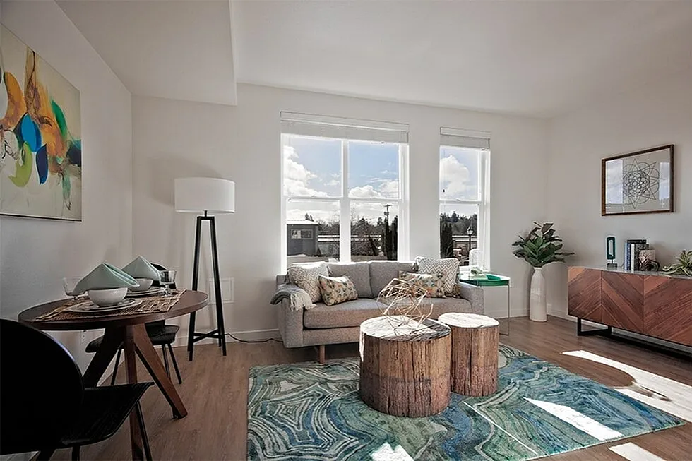 Bright and modern living room with large windows, cozy grey sofa, chic wooden coffee tables, and colorful artwork creating a welcoming atmosphere.