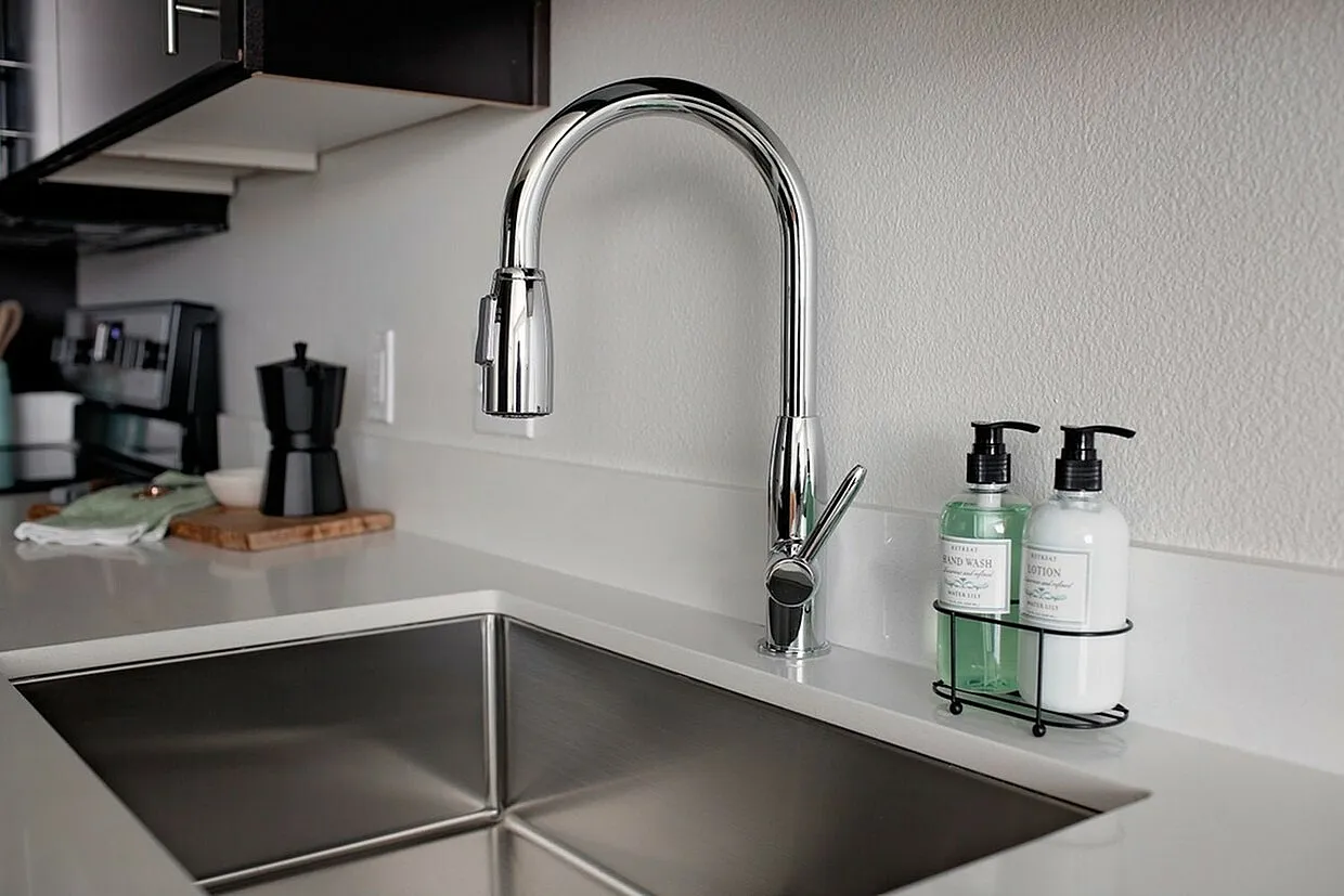 Modern kitchen sink with sleek chrome faucet, complemented by elegant soap and lotion dispensers on a pristine white countertop.