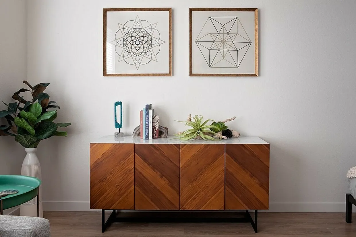 Elegant interior with a chic wooden cabinet, geometric wall art, and lush greenery, creating a modern and inviting ambiance.