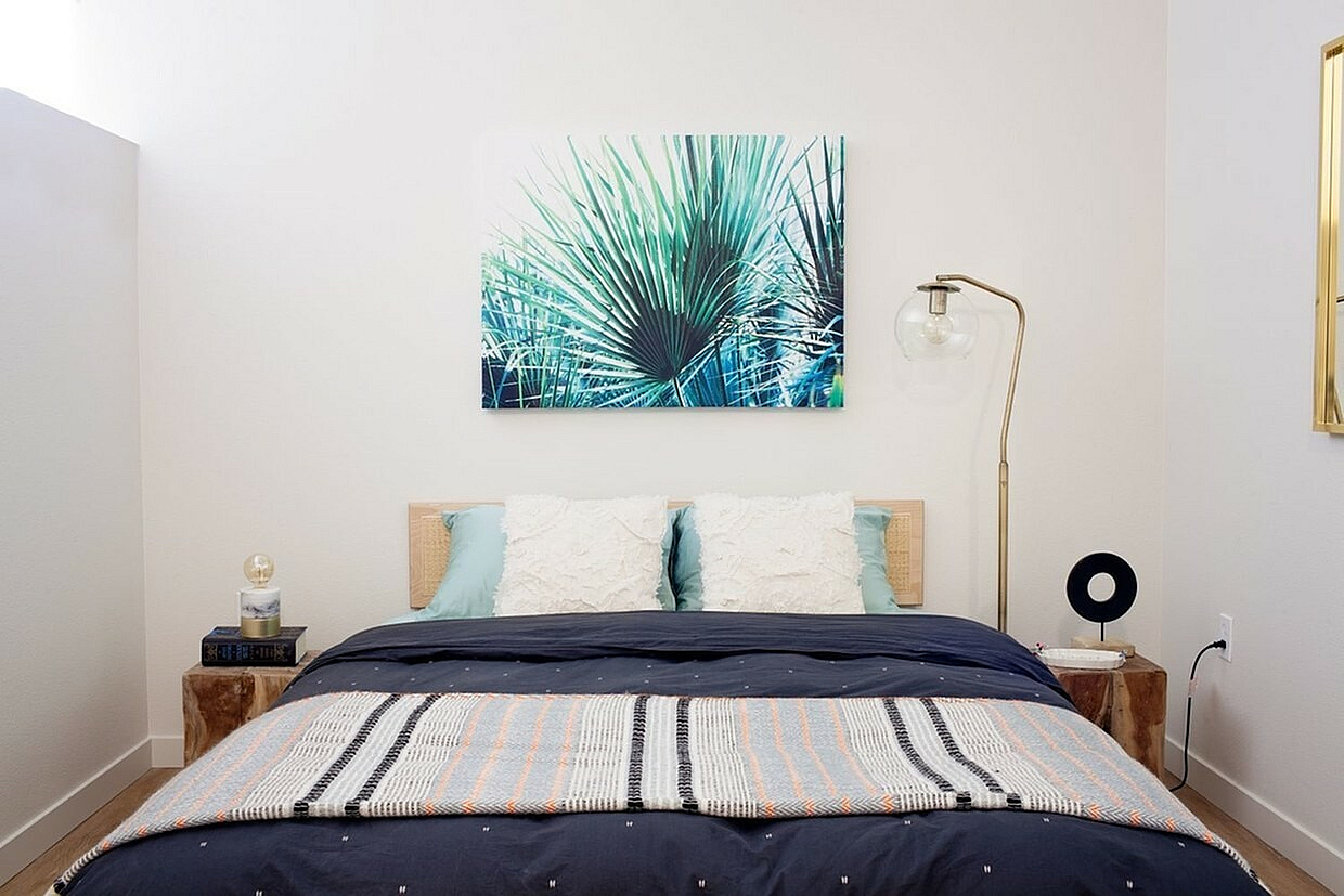 Chic apartment bedroom with modern decor, featuring a cozy bed, stylish floor lamp, and vibrant palm artwork creating a serene ambiance.