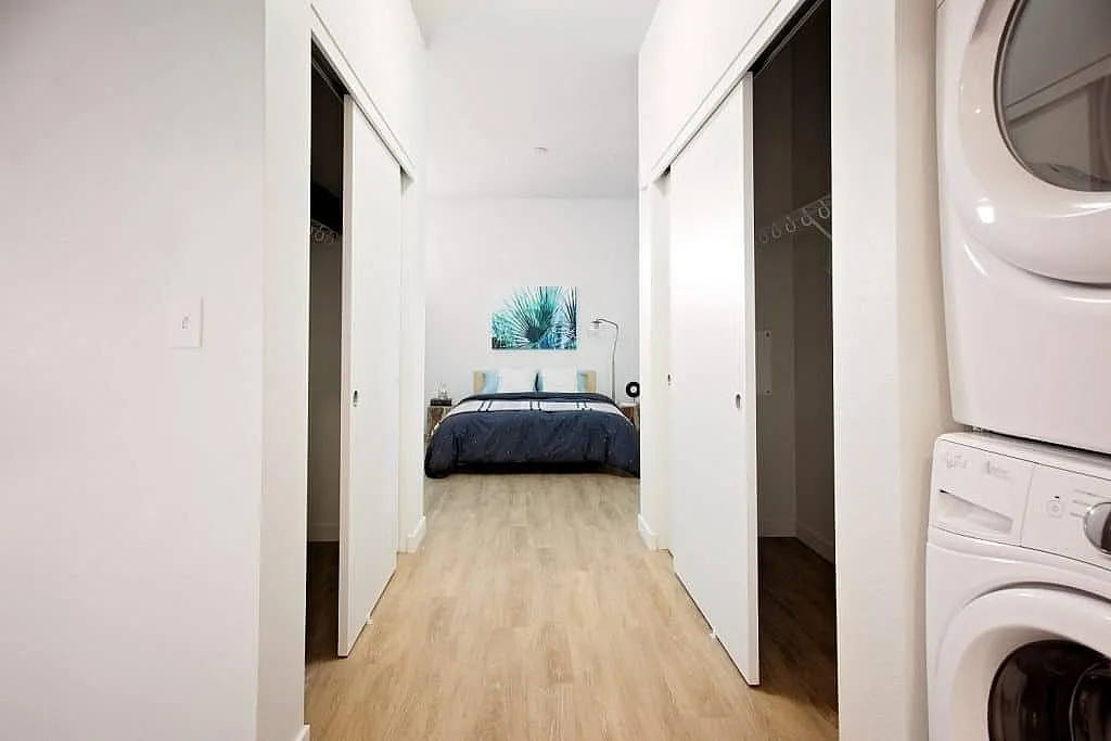 Inviting hallway leading to a cozy bedroom with hardwood floors and convenient in-unit laundry appliances.