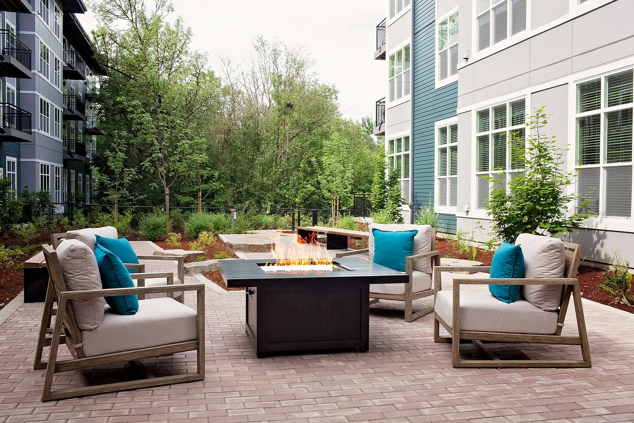 Chic apartment patio featuring cozy seating around a modern fire pit, surrounded by lush greenery and elegant architecture.
