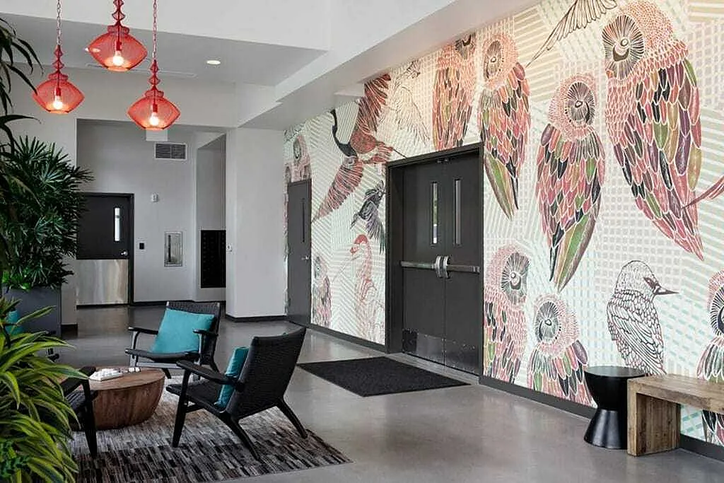 Vibrant lobby with artistic bird mural, chic seating area, and elegant red pendant lights offering a welcoming ambiance.