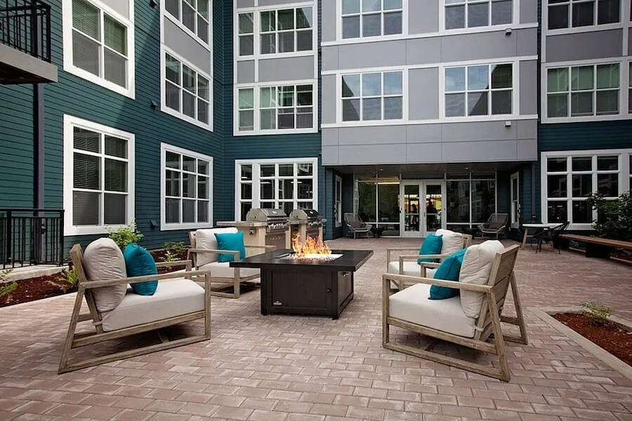 Modern apartment courtyard with cozy seating around a stylish fire pit, surrounded by elegant architecture and lush greenery.