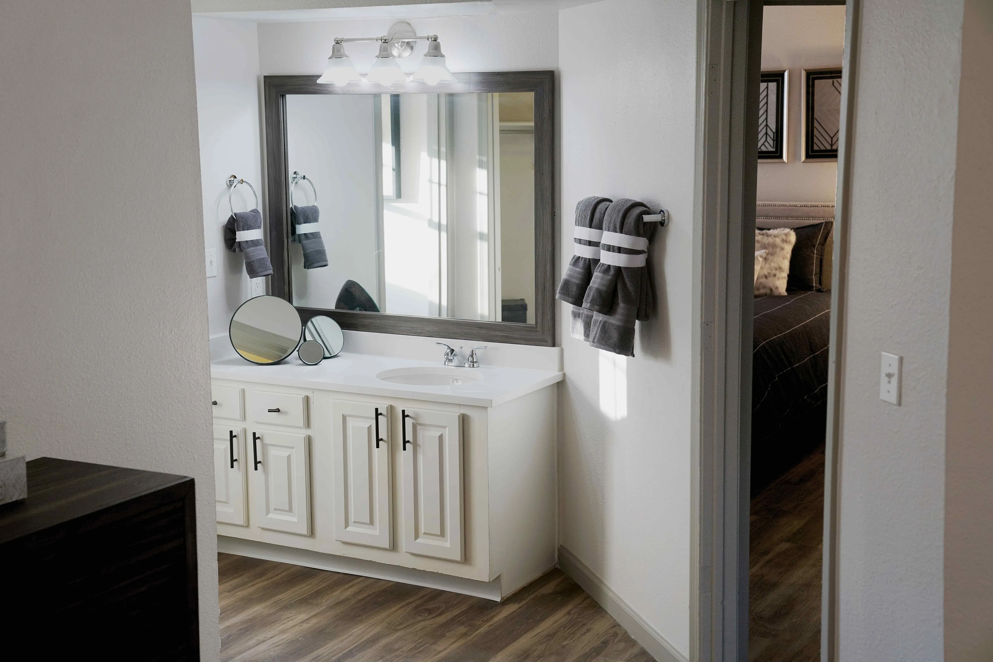 Elegant bathroom with a large mirror, modern vanity, and plush towels, leading to a cozy bedroom with stylish decor.
