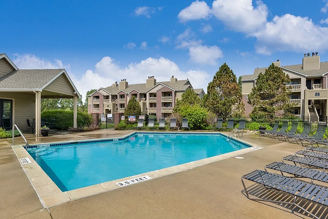 Inviting apartment complex with pristine swimming pool, sun loungers, and lush greenery under a bright blue sky.