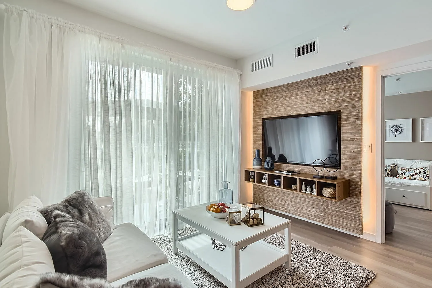 Cozy modern living room featuring elegant sheer curtains, a plush sofa, and a stylish entertainment unit with a mounted TV.