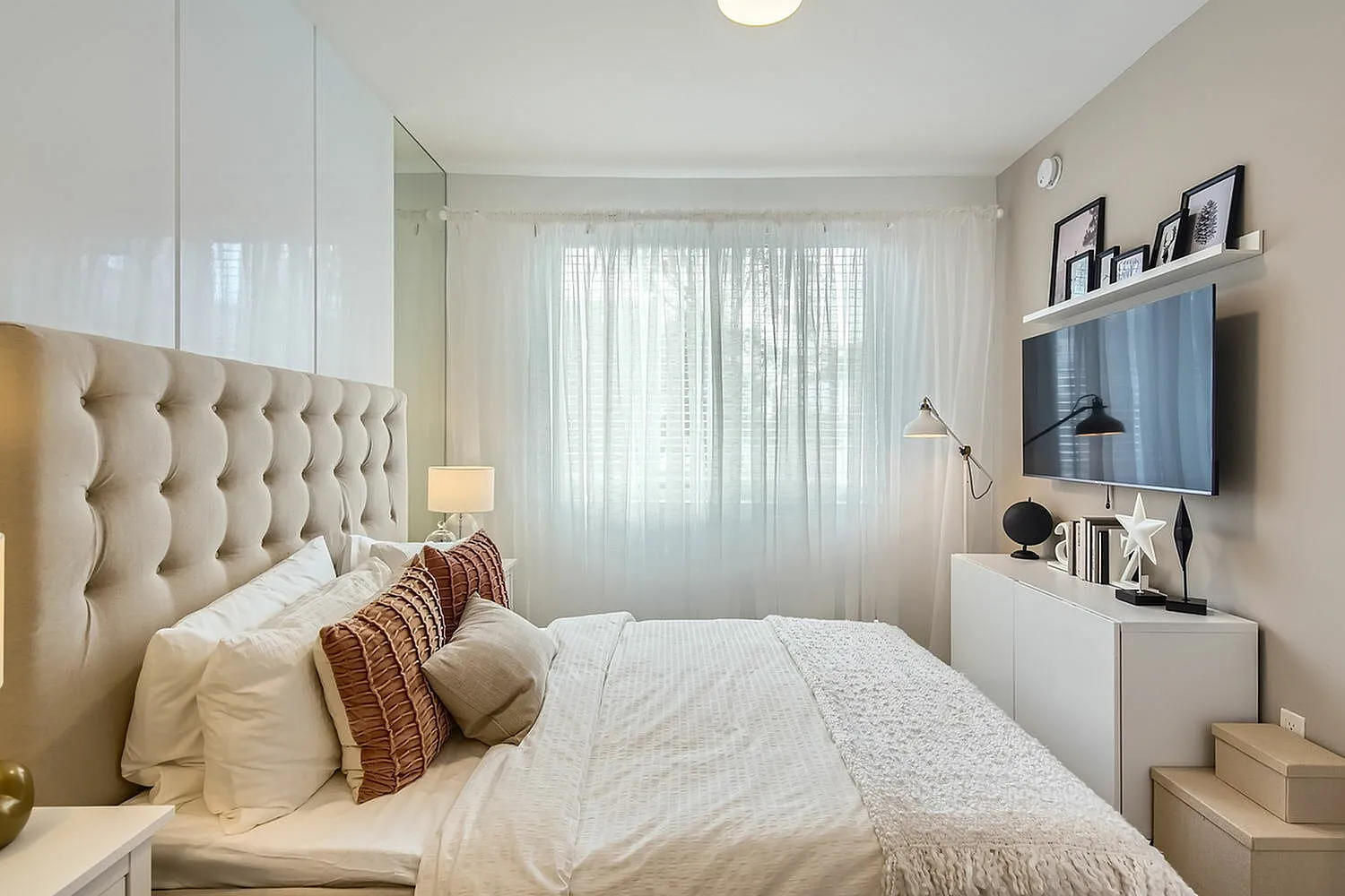 Elegant bedroom featuring a plush tufted headboard, ambient lighting, and stylish decor with a modern wall-mounted TV.