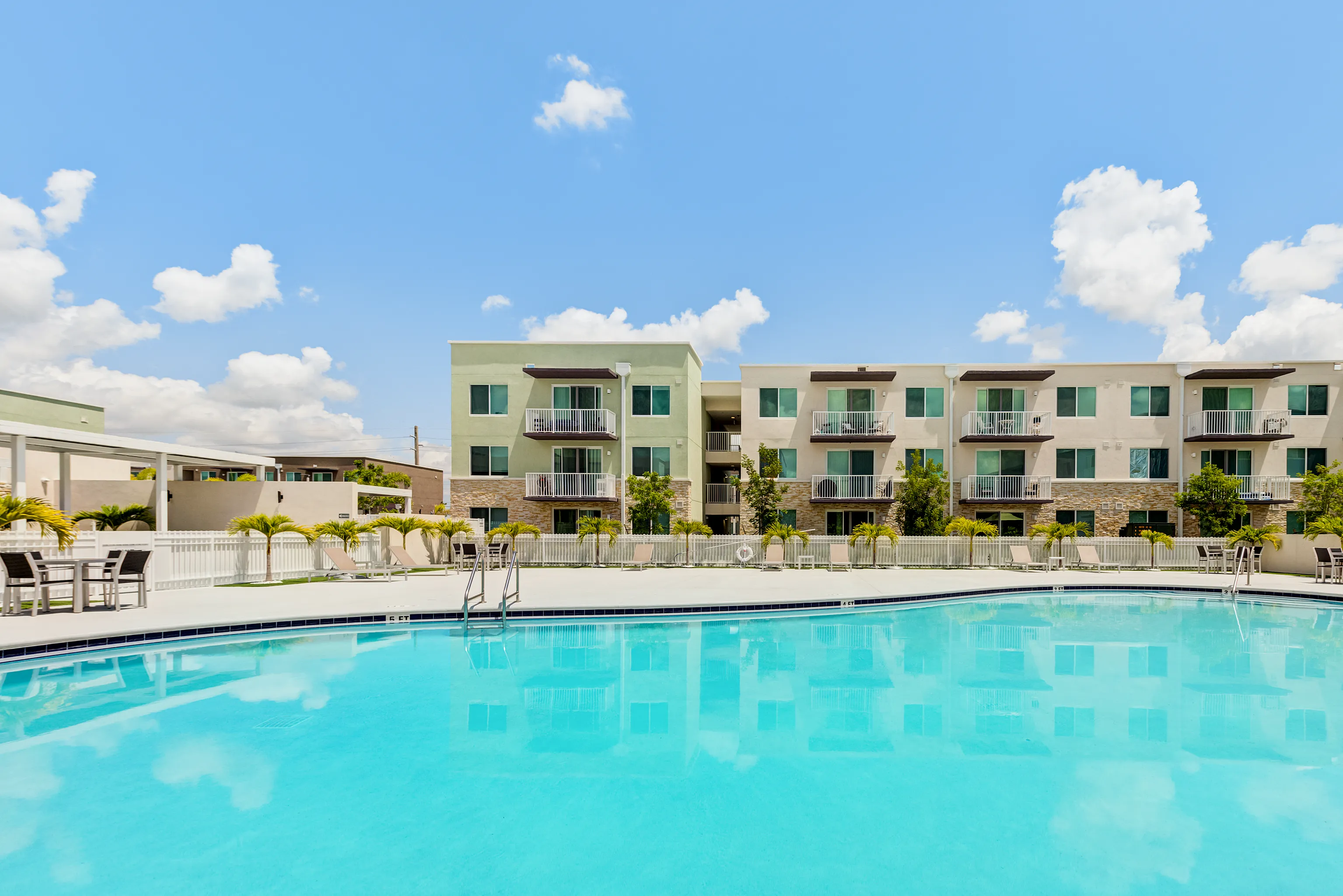 Inviting luxury apartments with private balconies overlook a sparkling pool, framed by clear blue skies.
