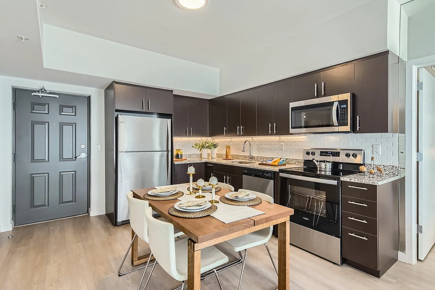 Modern kitchen with sleek dark cabinets, stainless steel appliances, and a cozy dining area with elegant table setting.