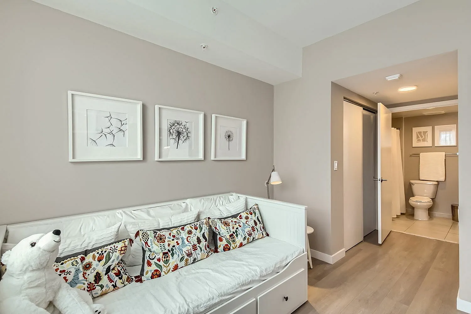 Charming bedroom with a cozy daybed, colorful pillows, and elegant monochrome artwork, featuring a modern en-suite bathroom.