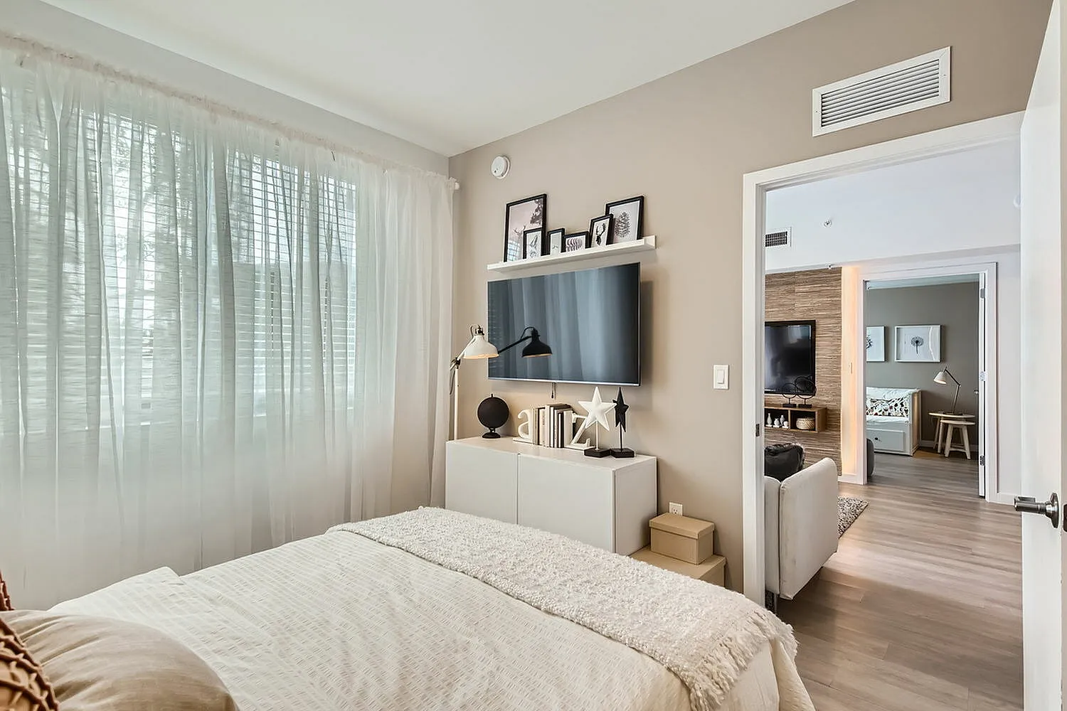 Inviting bedroom with large windows, elegant decor, and a cozy ambiance flowing into a stylish living space.