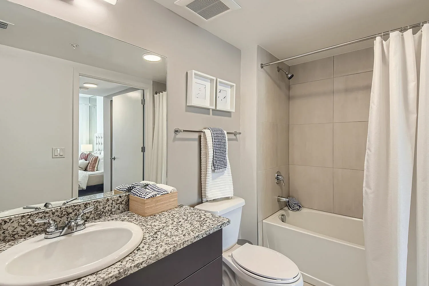 Modern bathroom with elegant granite countertop, stylish fixtures, and a cozy bathtub, offering a glimpse into a luxurious bedroom.
