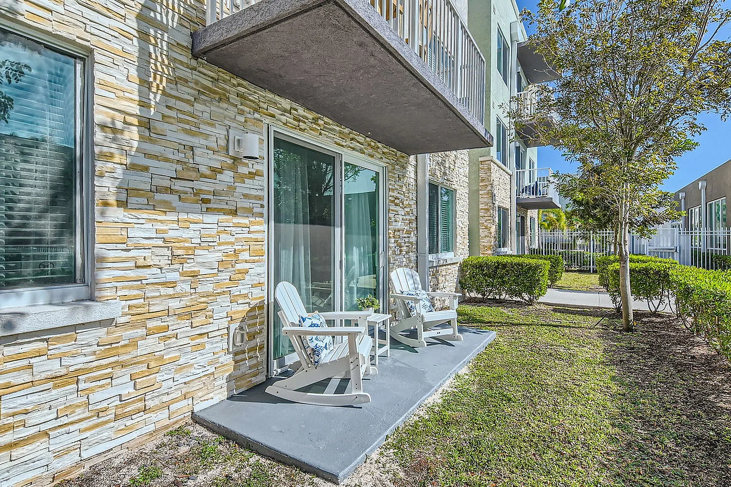 Charming apartment patio with stone facade, two inviting rocking chairs, and lush garden views.