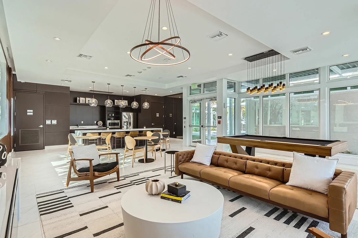 Modern and stylish open-concept living space featuring luxury seating, a sleek kitchen with pendant lighting, and an elegant billiards table.