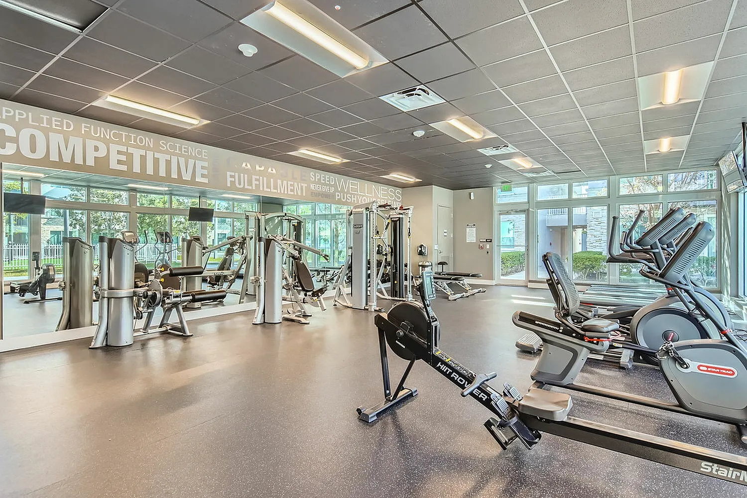 Bright and modern fitness center with state-of-the-art equipment and large windows overlooking lush greenery, offering an inviting space for a perfect workout.