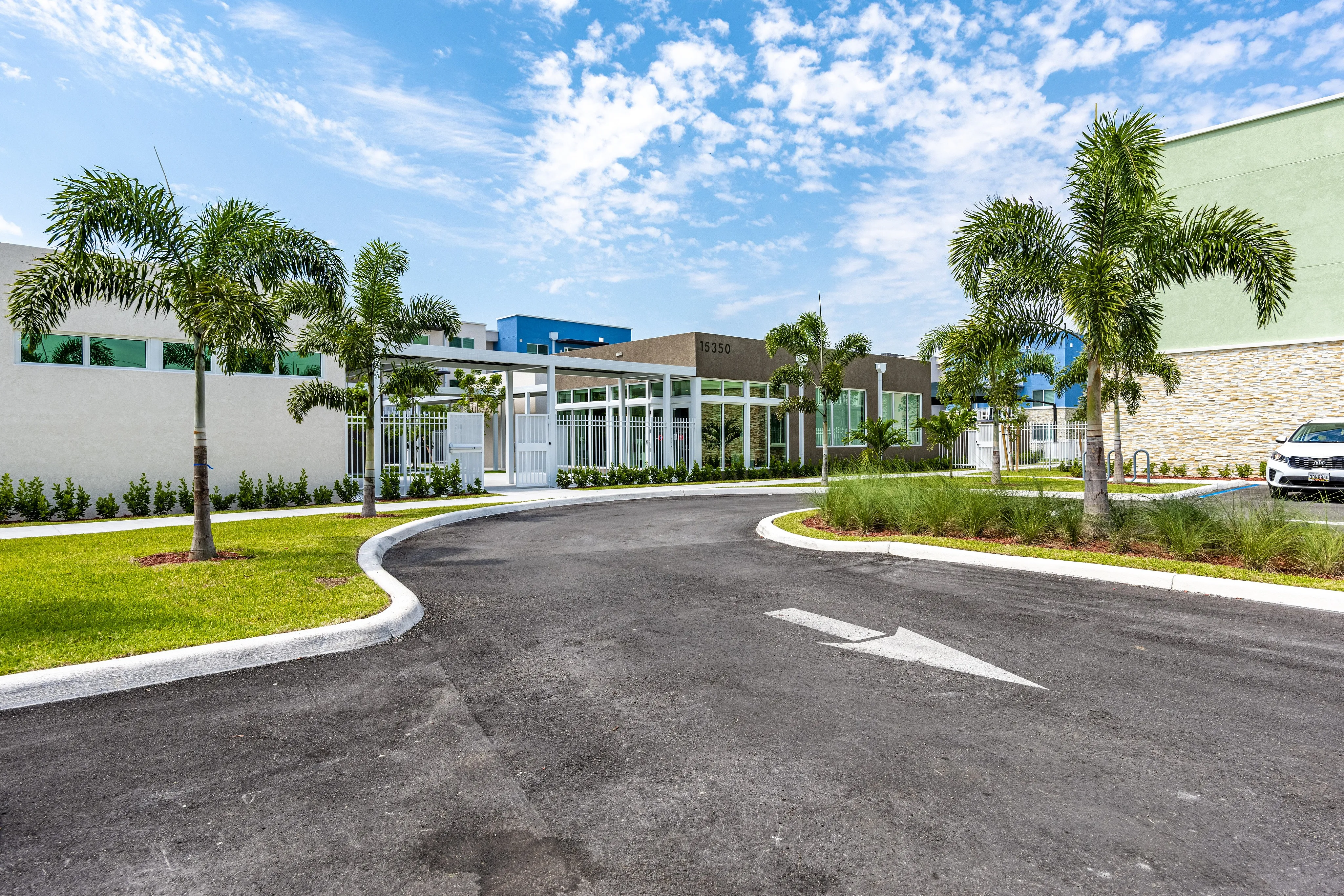 Inviting entrance to a modern apartment complex, featuring lush palm trees and a bright, welcoming pathway.