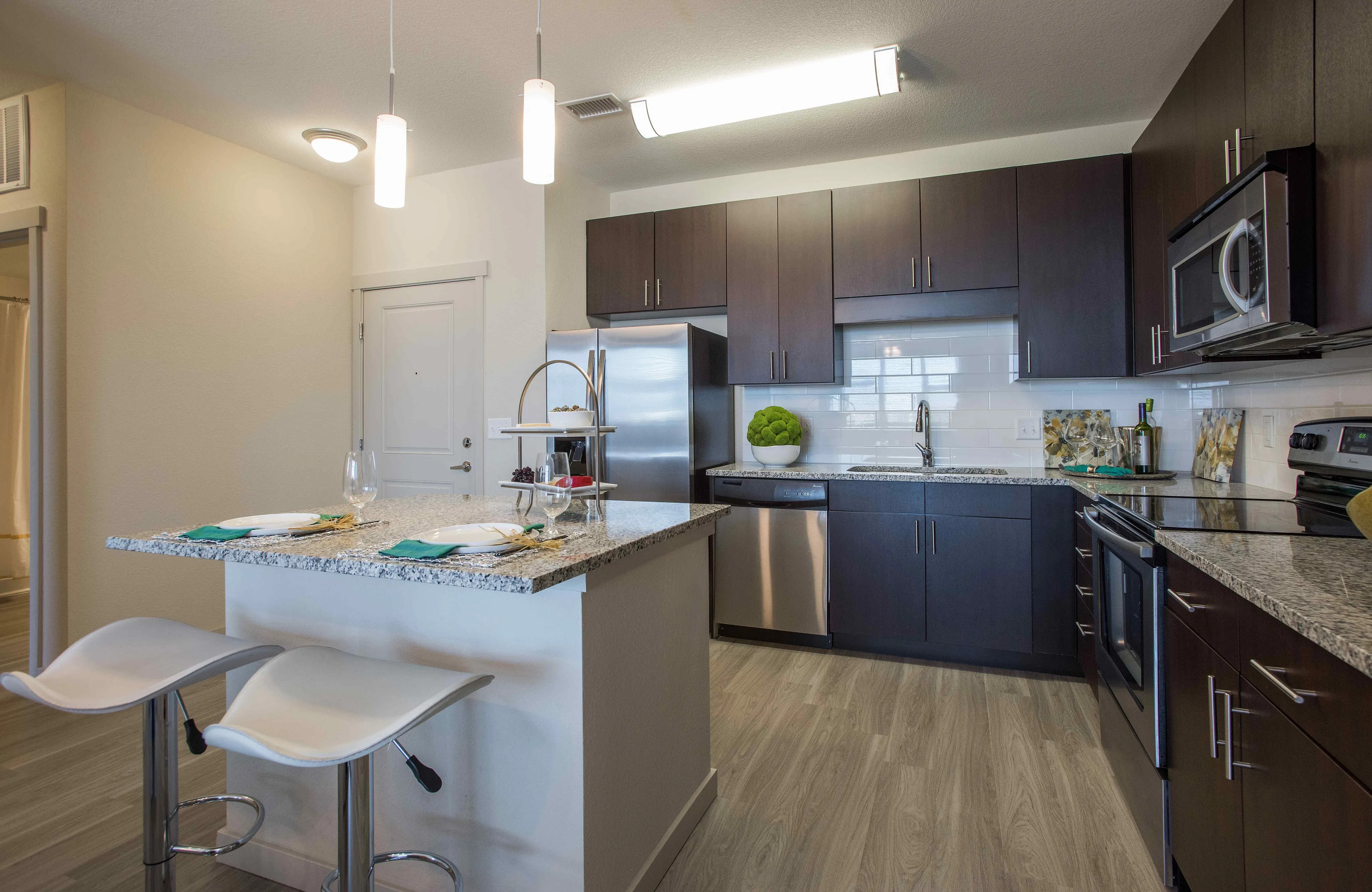Modern kitchen with sleek dark cabinets, granite countertops, and stainless steel appliances, featuring a cozy breakfast bar with stylish stools.