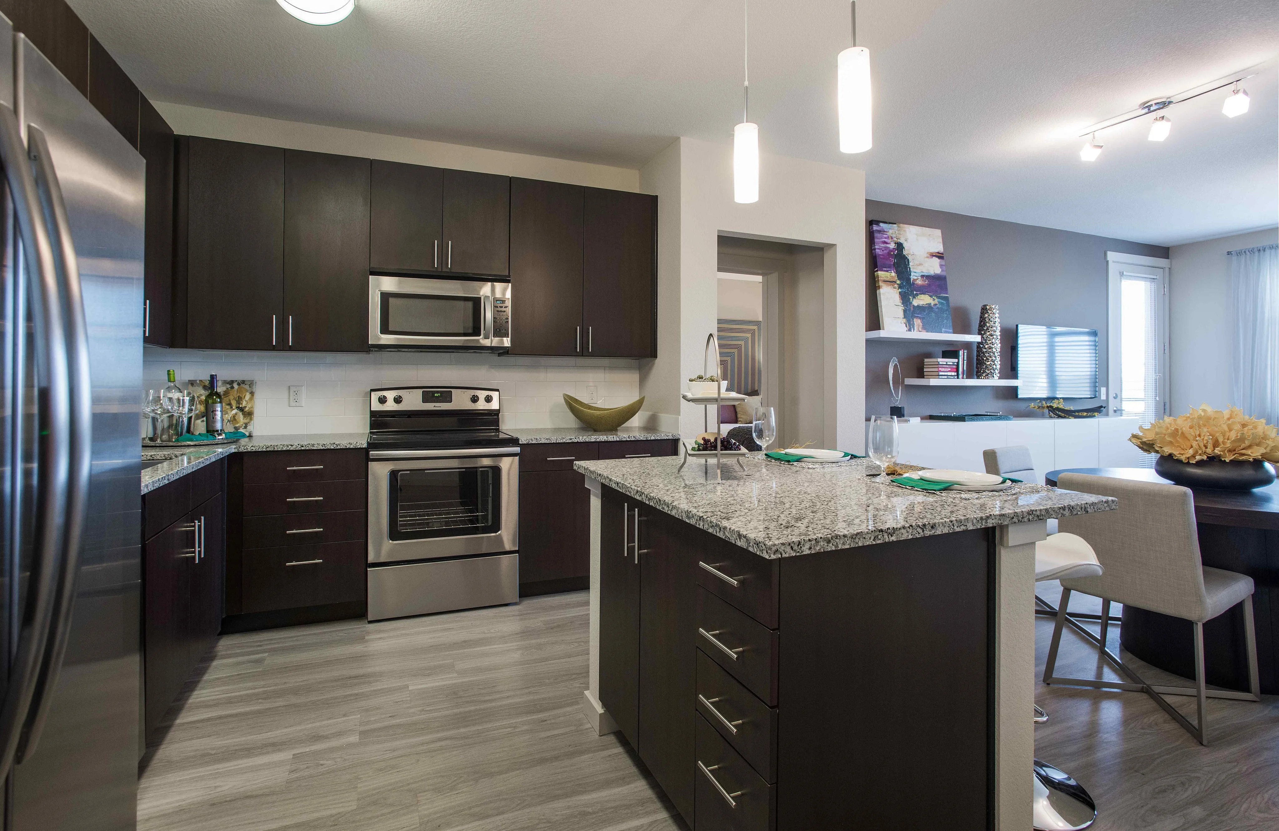 Modern kitchen featuring sleek dark wood cabinets, granite countertops, and stainless steel appliances, opening into a stylish dining area for luxurious living.