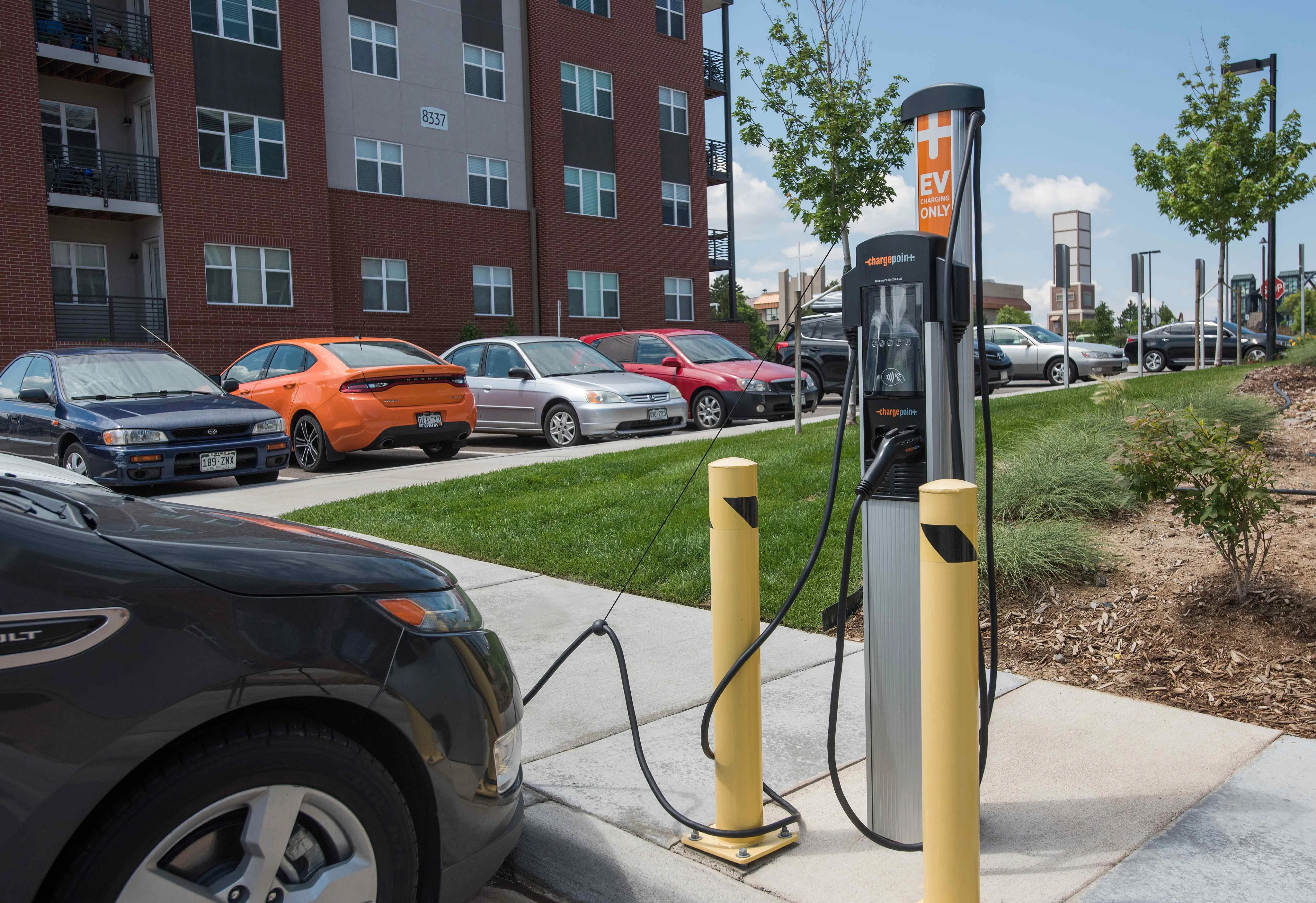 Modern apartment building with convenient EV charging station in the parking area, surrounded by well-kept landscaping.