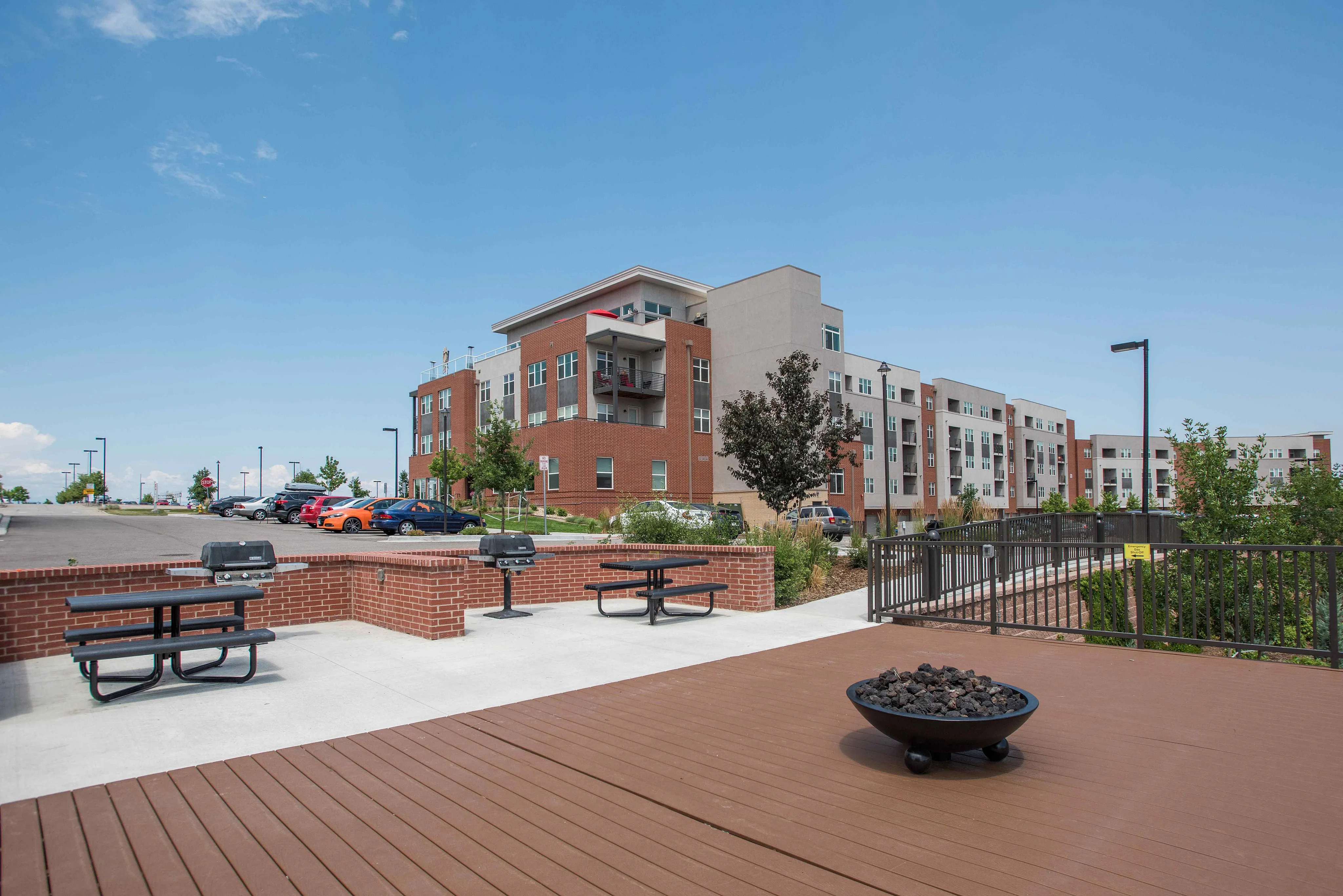 Modern apartment complex with brick facade, outdoor seating, and vibrant landscaping under clear blue skies.