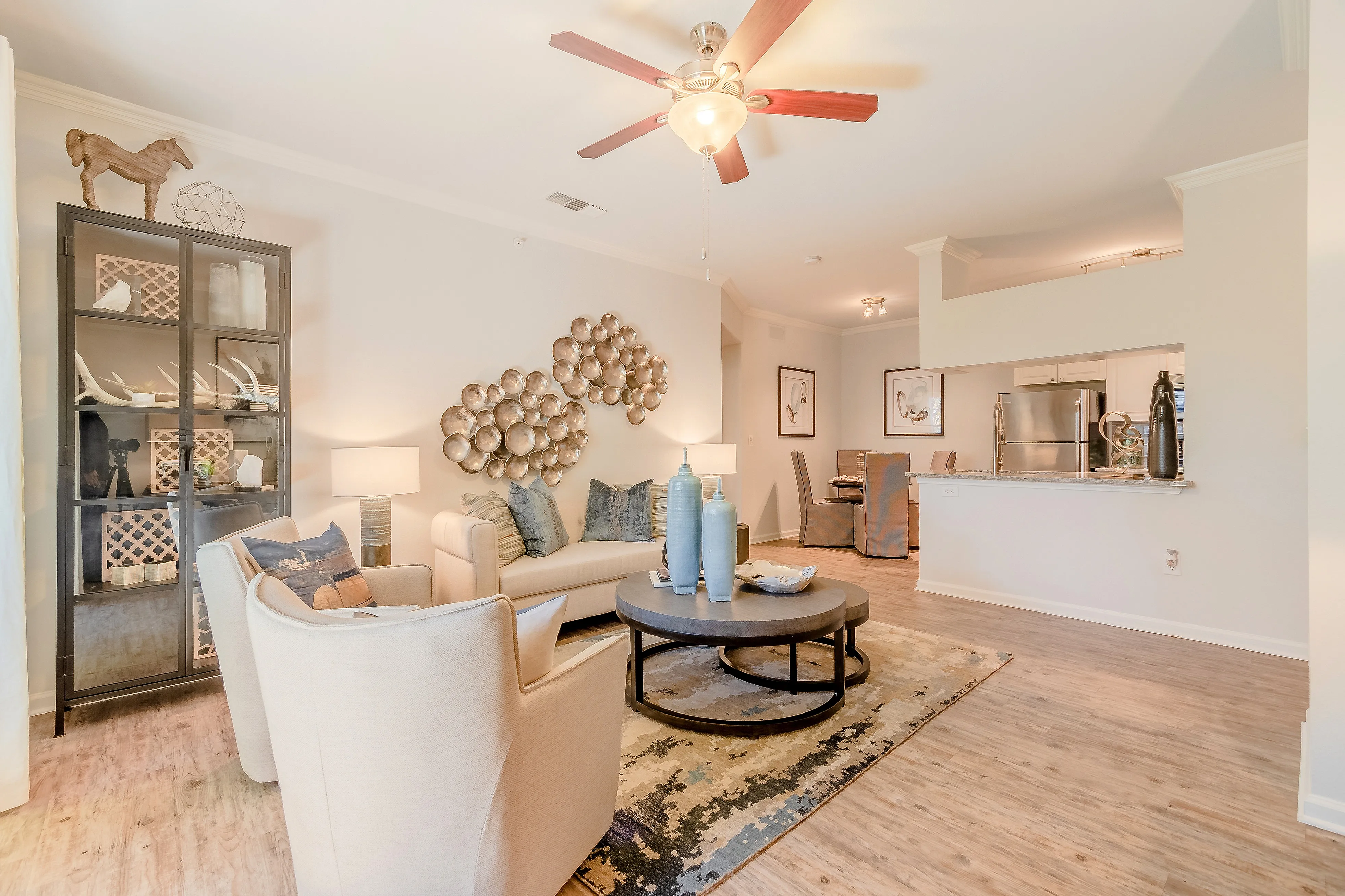 Charming living room with elegant decor, featuring cozy beige seating, modern light fixtures, and an open kitchen view. Perfect for relaxation and entertaining.