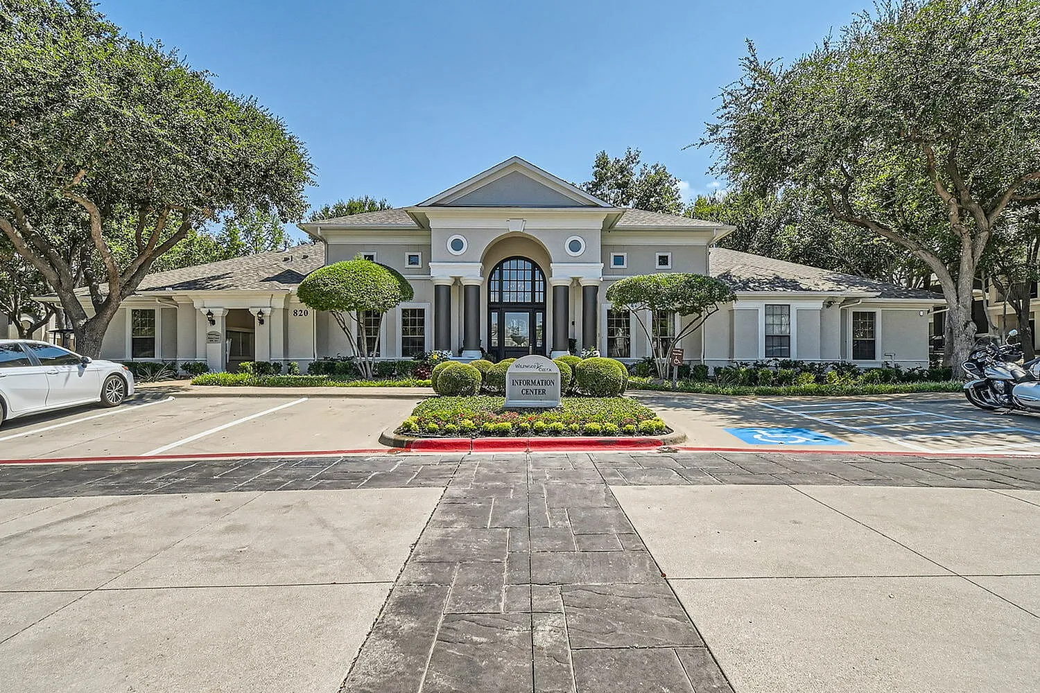 Elegant apartment complex entrance with grand architecture, manicured landscaping, and inviting information center.