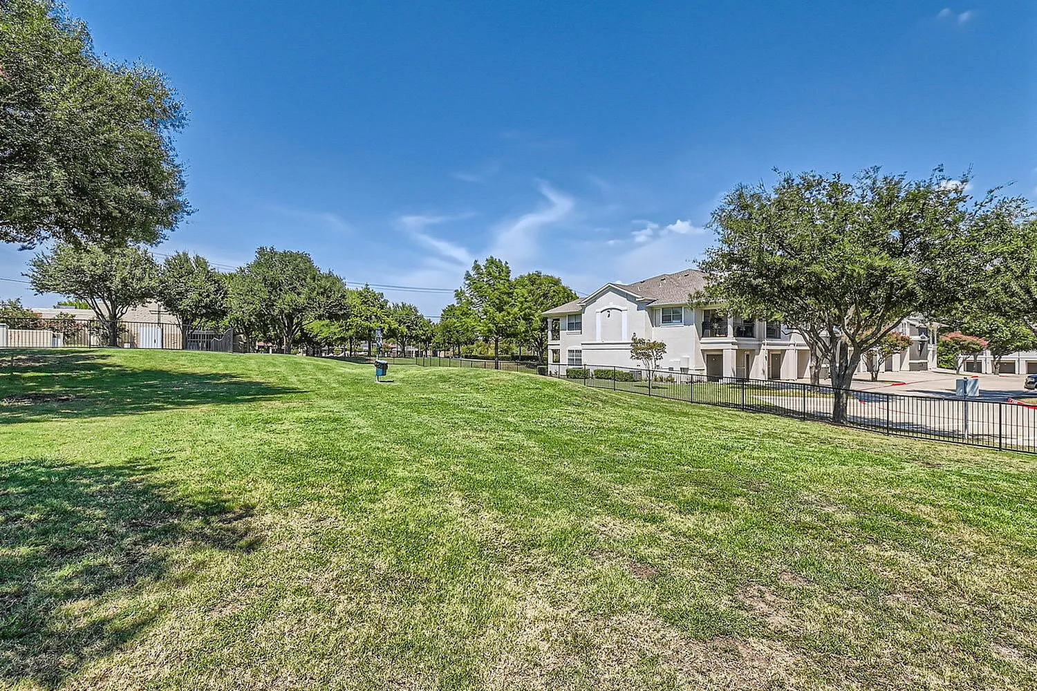 Lush green landscape surrounding modern apartment buildings under a clear blue sky, offering serene outdoor living.