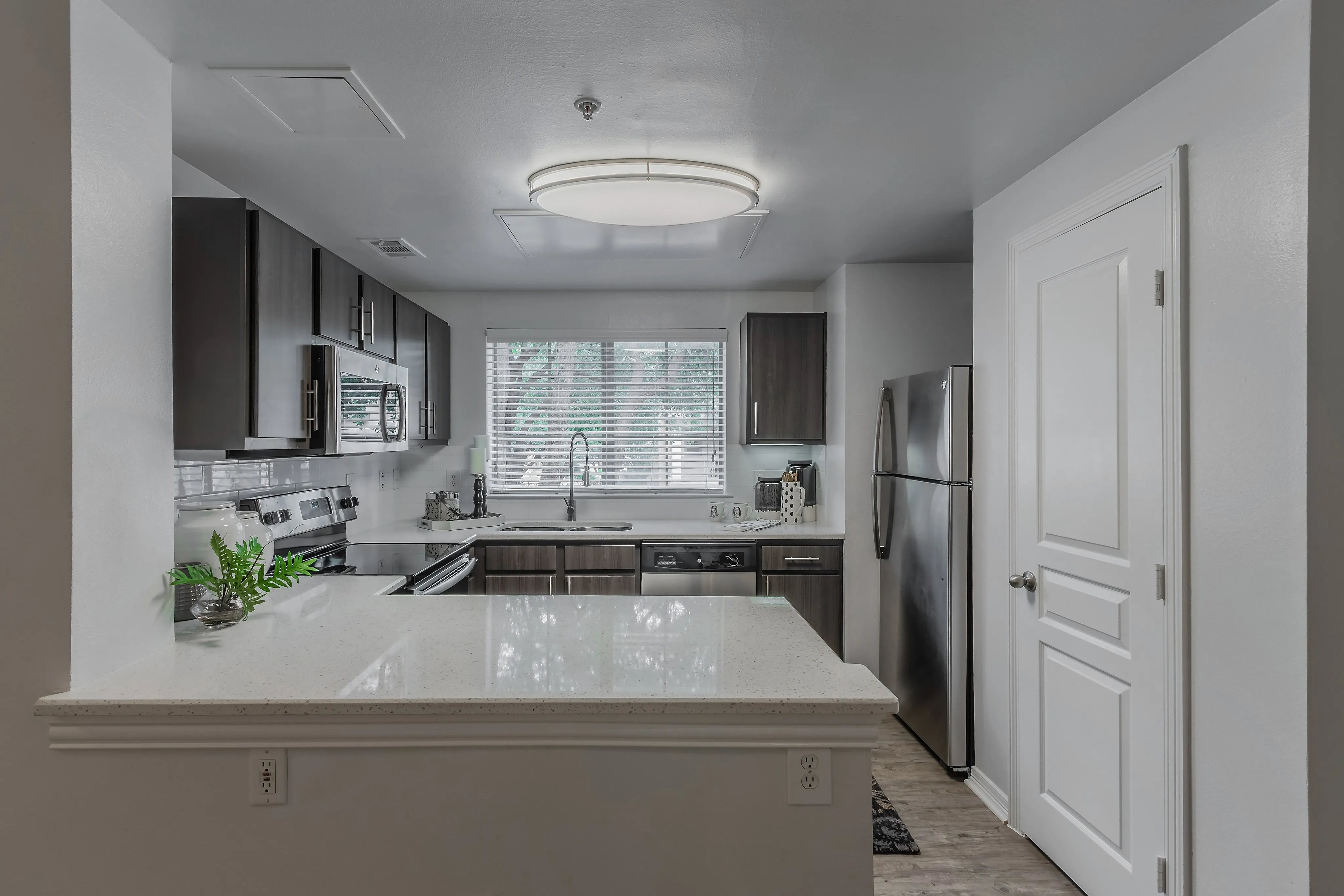 Modern kitchen with sleek dark cabinets, stainless steel appliances, and a spacious countertop, accented by natural light through a large window.